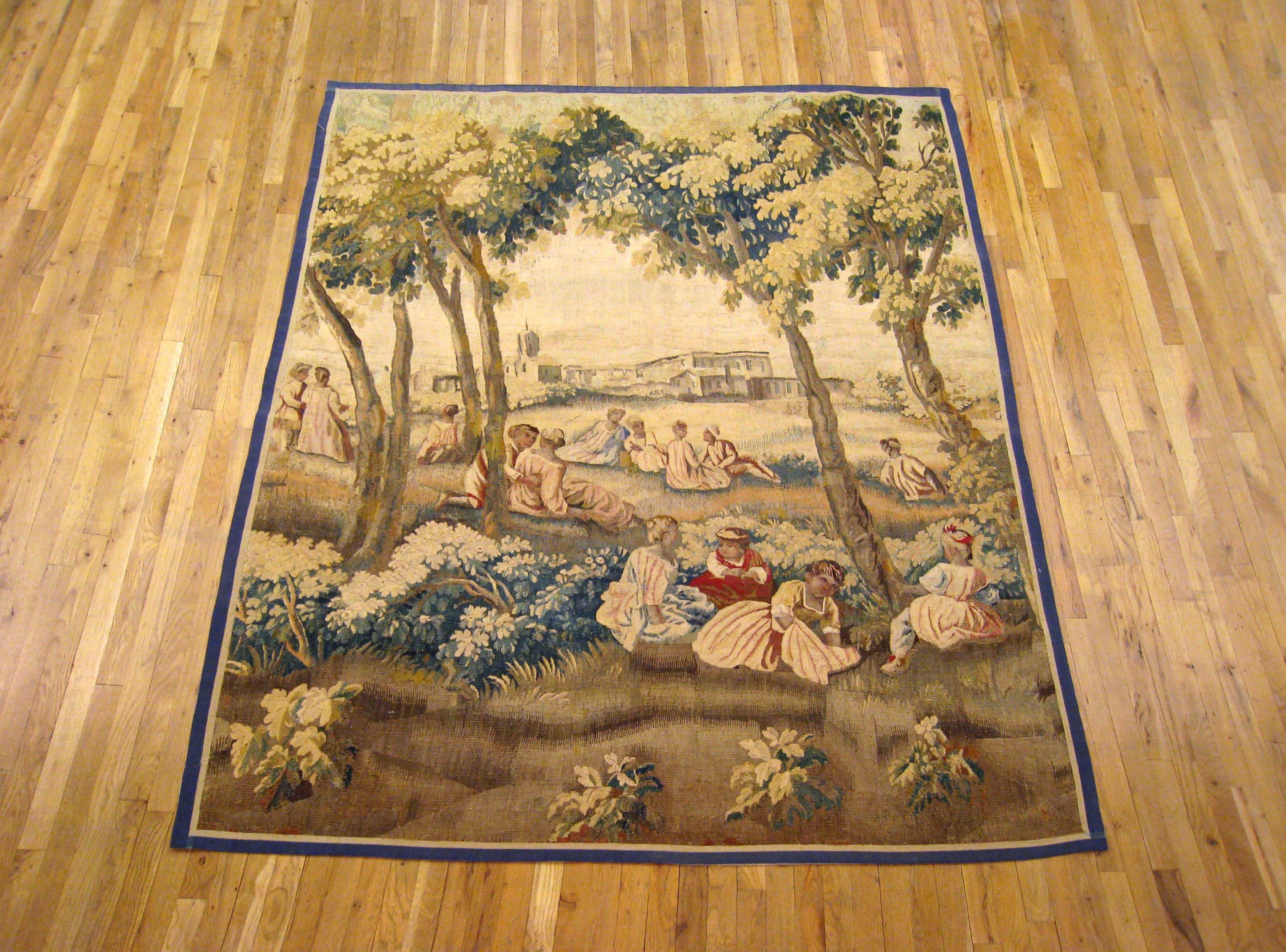 A French Aubusson rustic tapestry panel from the 18th century, featuring several women and children in the foreground, tending to various chores while seated in a grassy field, with several other people in the background facing the elegant