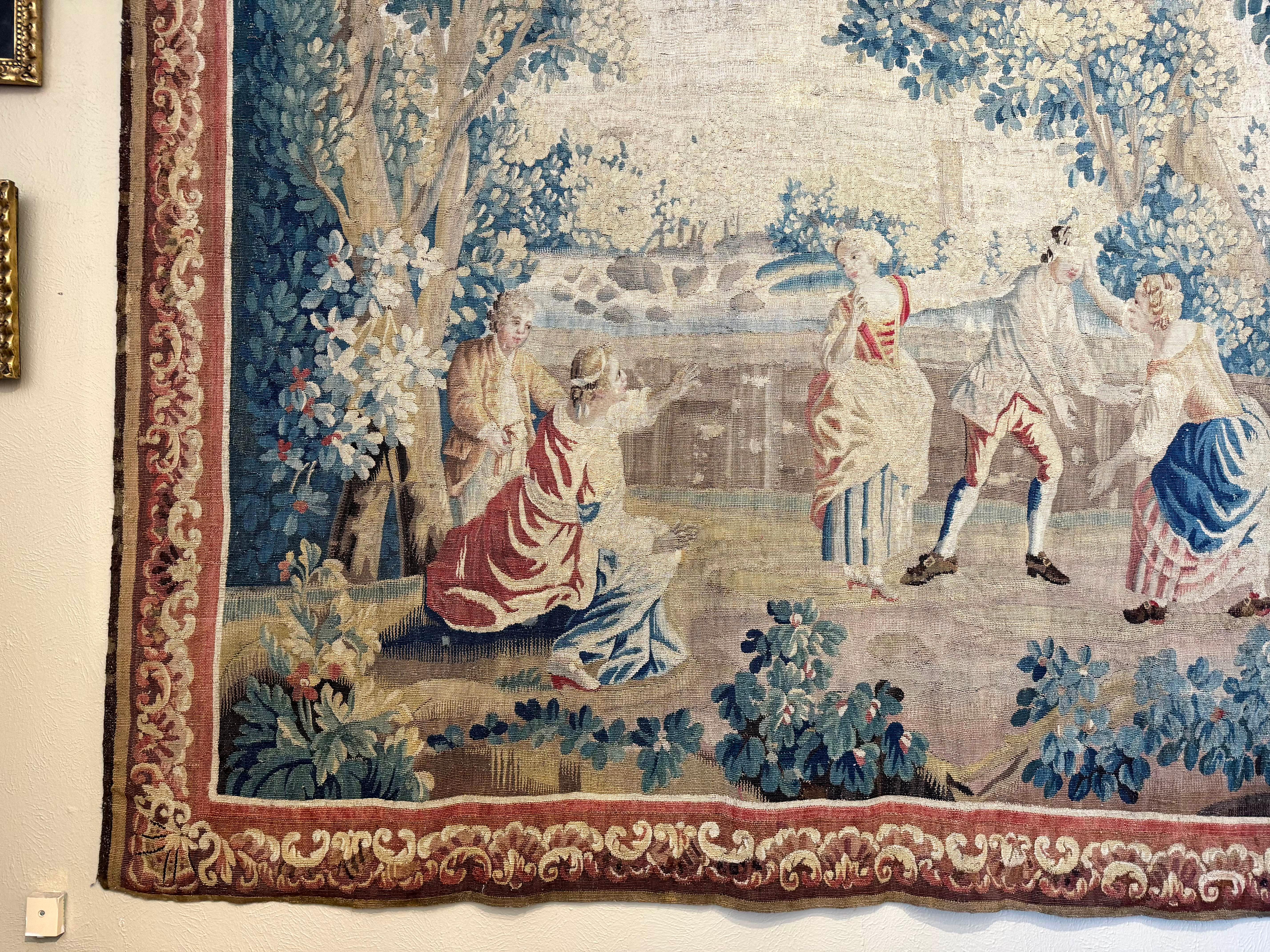 This large and elegant antique tapestry was woven in Aubusson, France, circa 1760. The handwoven scene depicts a lively group of figures engaged in the popular 18th-century game Colin-Maillard (Blind Man’s Buff), set within a lush wooded landscape