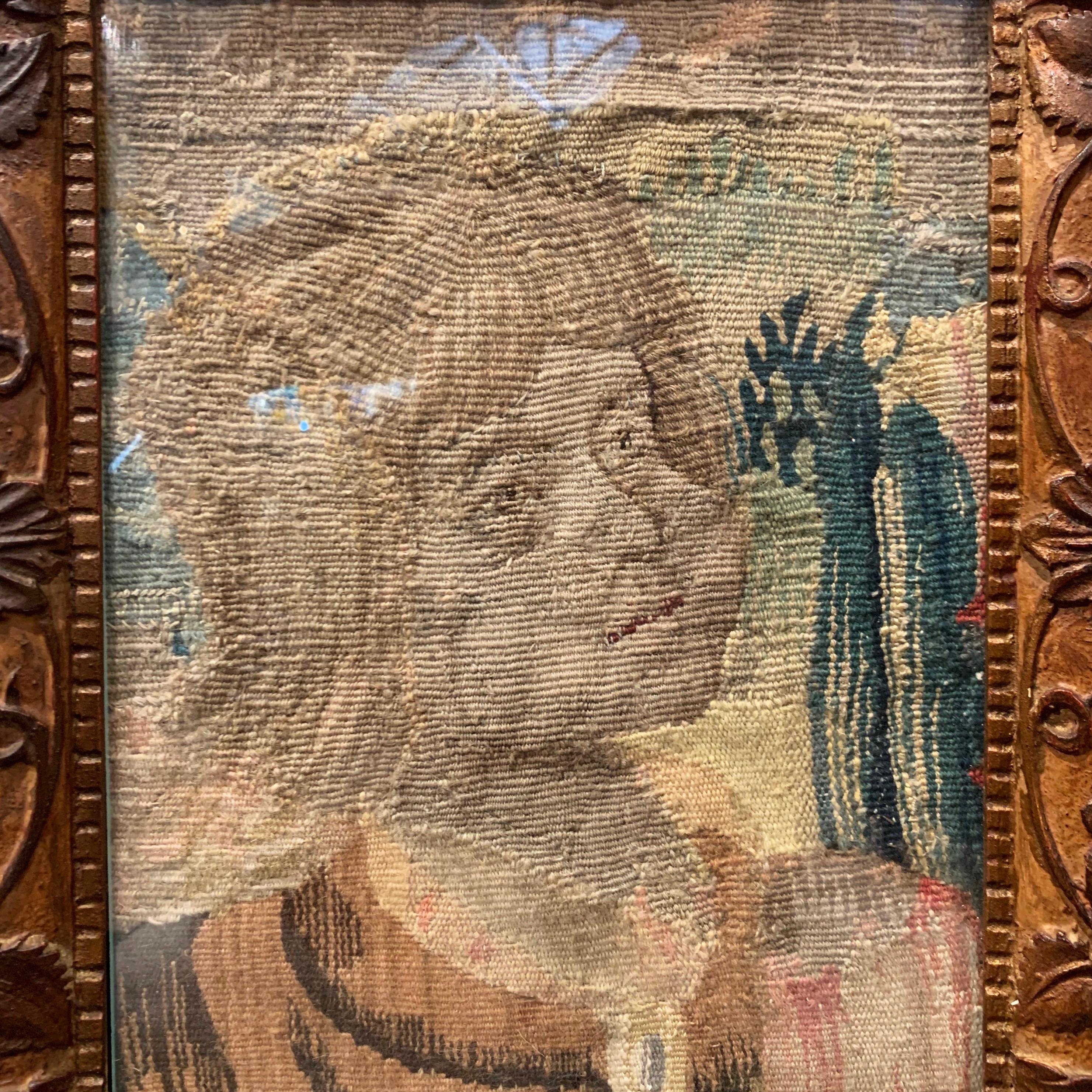 Set in a carved frame embellished with floral motifs, and protected with glass, the antique Aubusson fragment probably represents Joan of Arc at an early age. The wall decor is in excellent condition with rich colors on the beige, blue and brown