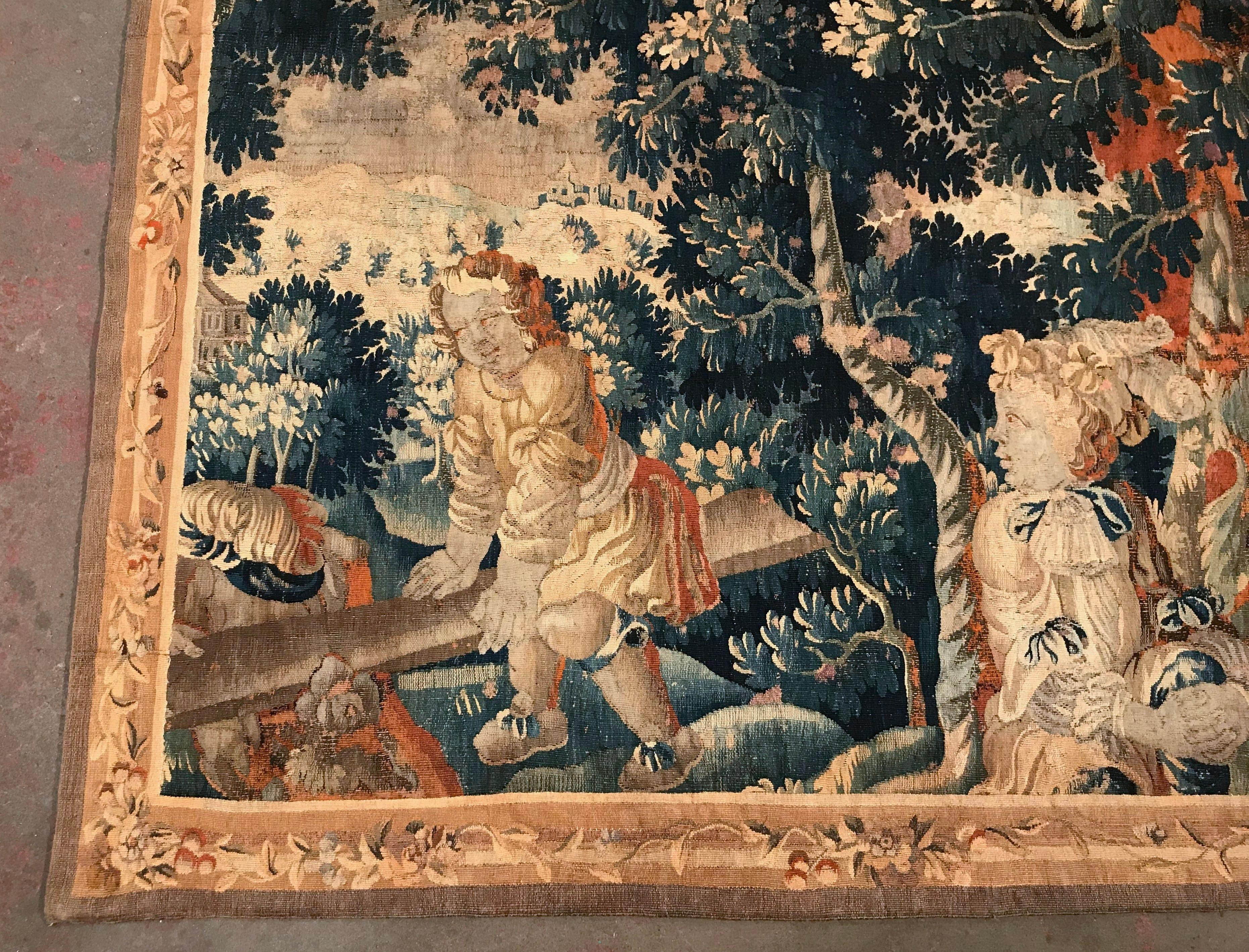 Handwoven in Aubusson, France, circa 1780, and set in a beige border decorated with floral motifs, the colorful wall piece features two young cheerful cherubs at play, one sited on a swing board, the other looking on. The tapestry is further