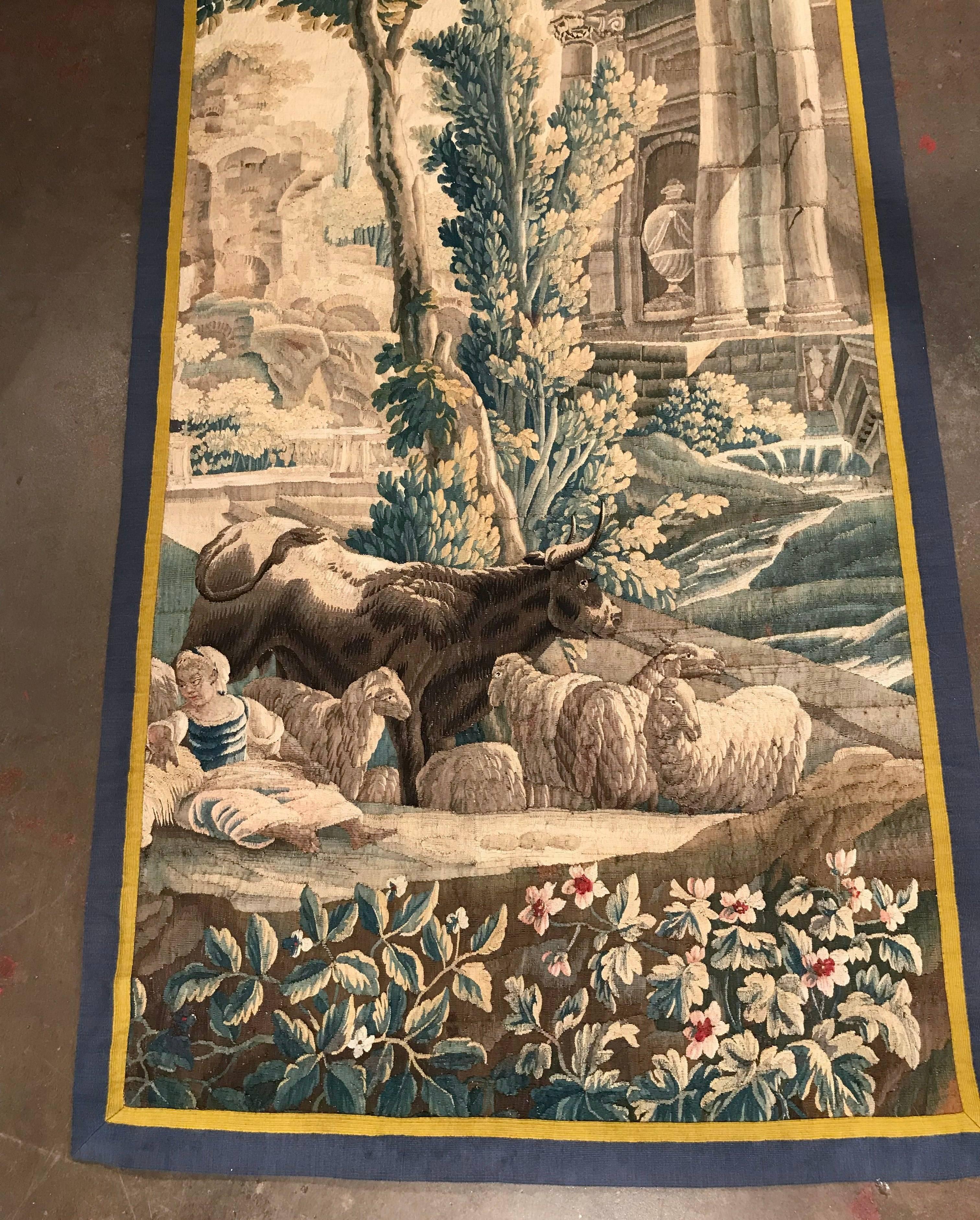 Place this long and narrow antique tapestry in a staircase or in between two windows for a pop of color. Handwoven in Aubusson, France, circa 1780, the colorful wall piece has a two-toned border and depicts a pastoral scene with five sheep, a bovine