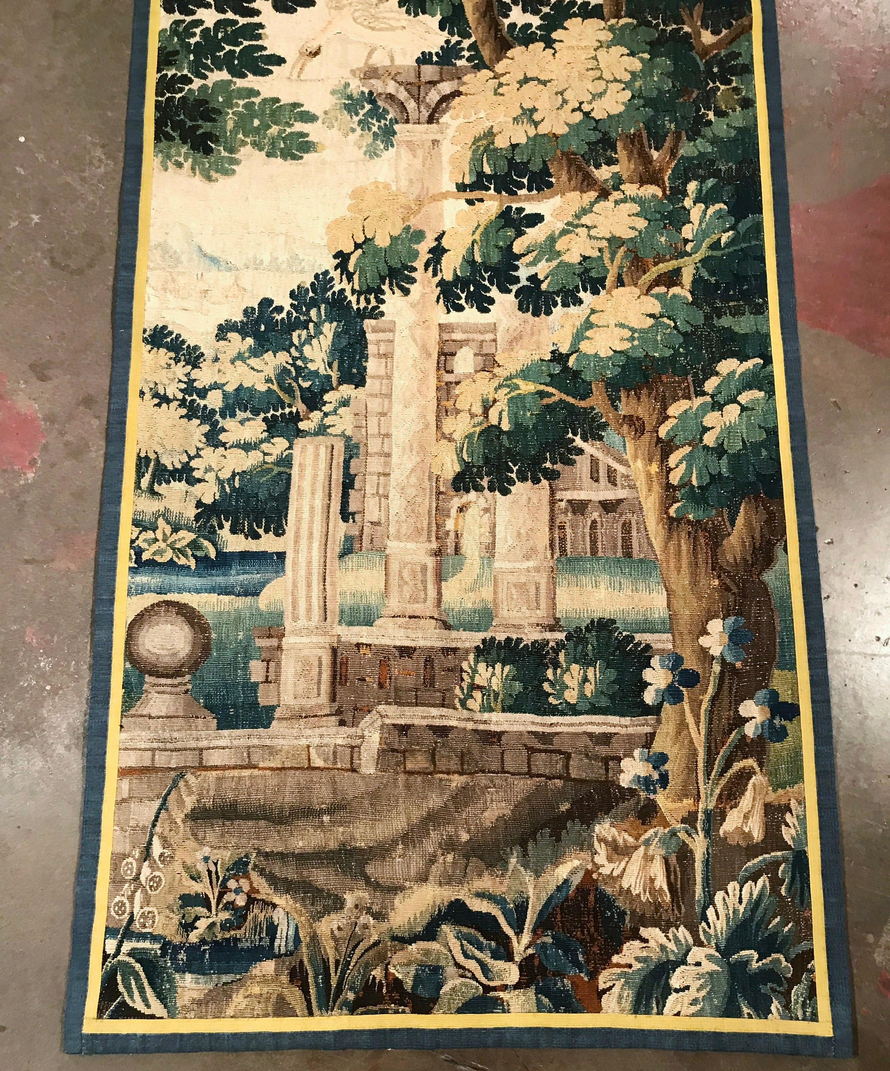 Place this long and narrow antique tapestry in a staircase or in between two windows for a pop of color. Handwoven in Aubusson, France, circa 1760, the verdure wall piece has a two-tone border, and features large trees with foliage and floral decor.