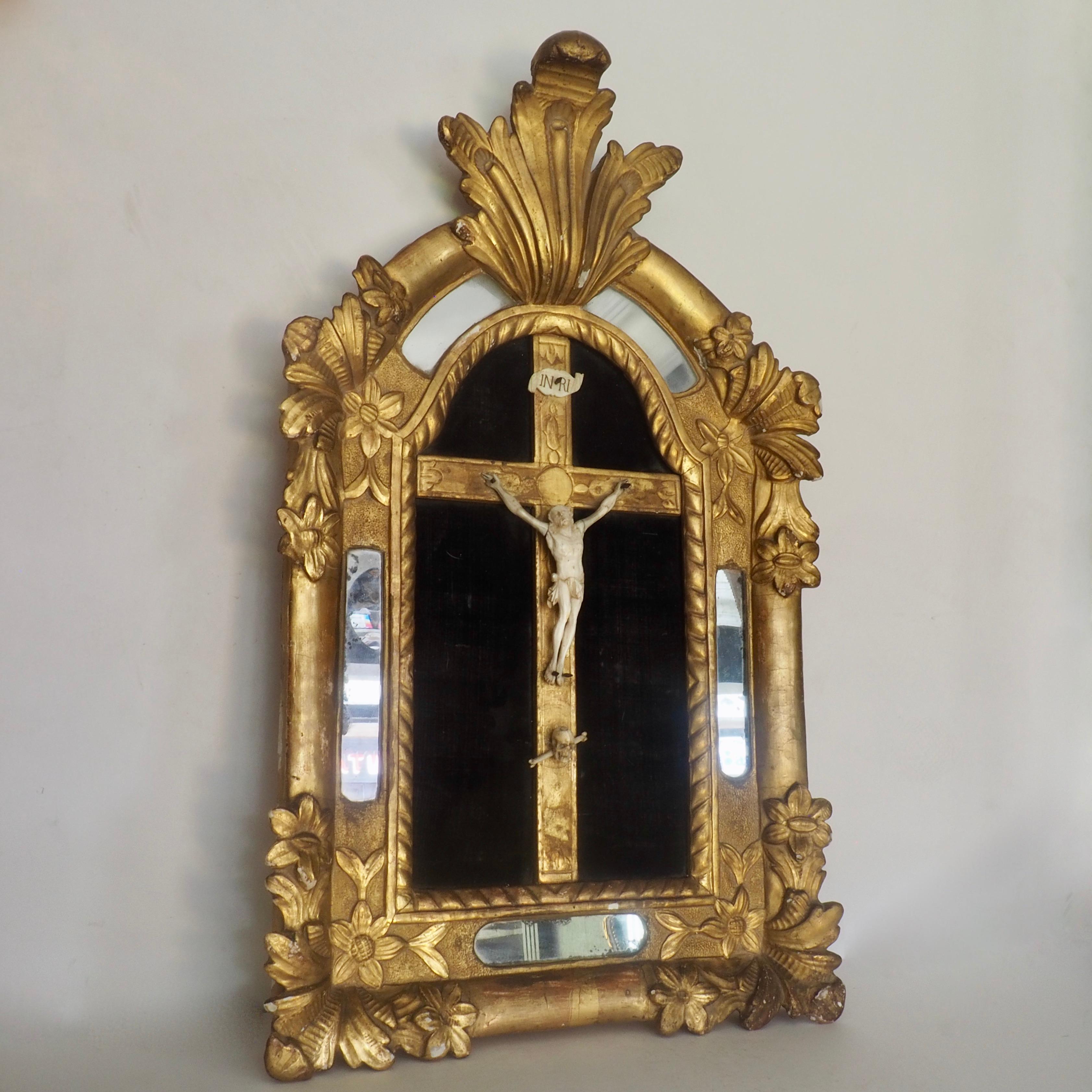 An early 18th century crucifix cushion mirror in the late baroque manner. Magnificently carved in giltwood and bone; the mirror depicts Christ on the cross laid onto black velvet, decorated with a deaths head device and surrounded by a giltwood