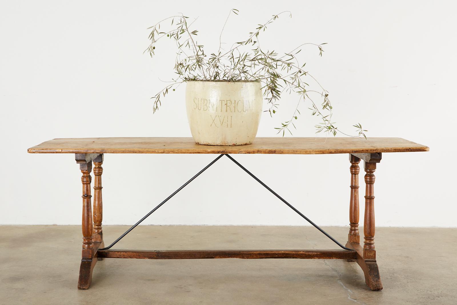 Elegant 18th century French Baroque dining or refectory table featuring iron trestle supports. The table is beautifully crafted from mixed woods with a lovely, aged rustic patina. The plank top is supported by turned oak legs and mounted to shoe