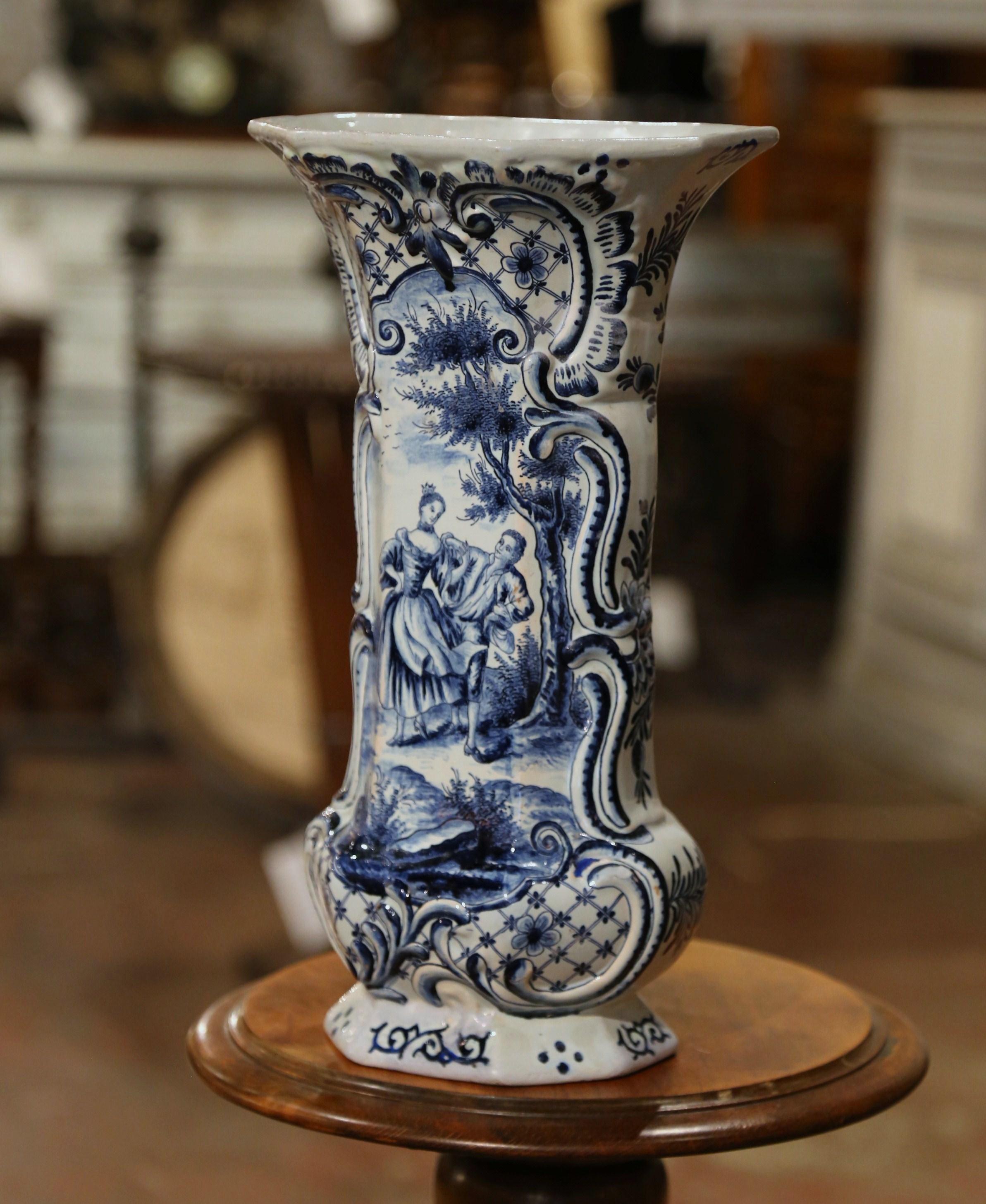 This important antique vase was crafted in France, circa 1780. Octagonal in shape with gadrooned body style and a tall neck, the elegant potiche features a hand painted medallion depicting an outdoor courting scene in the traditional blue and white