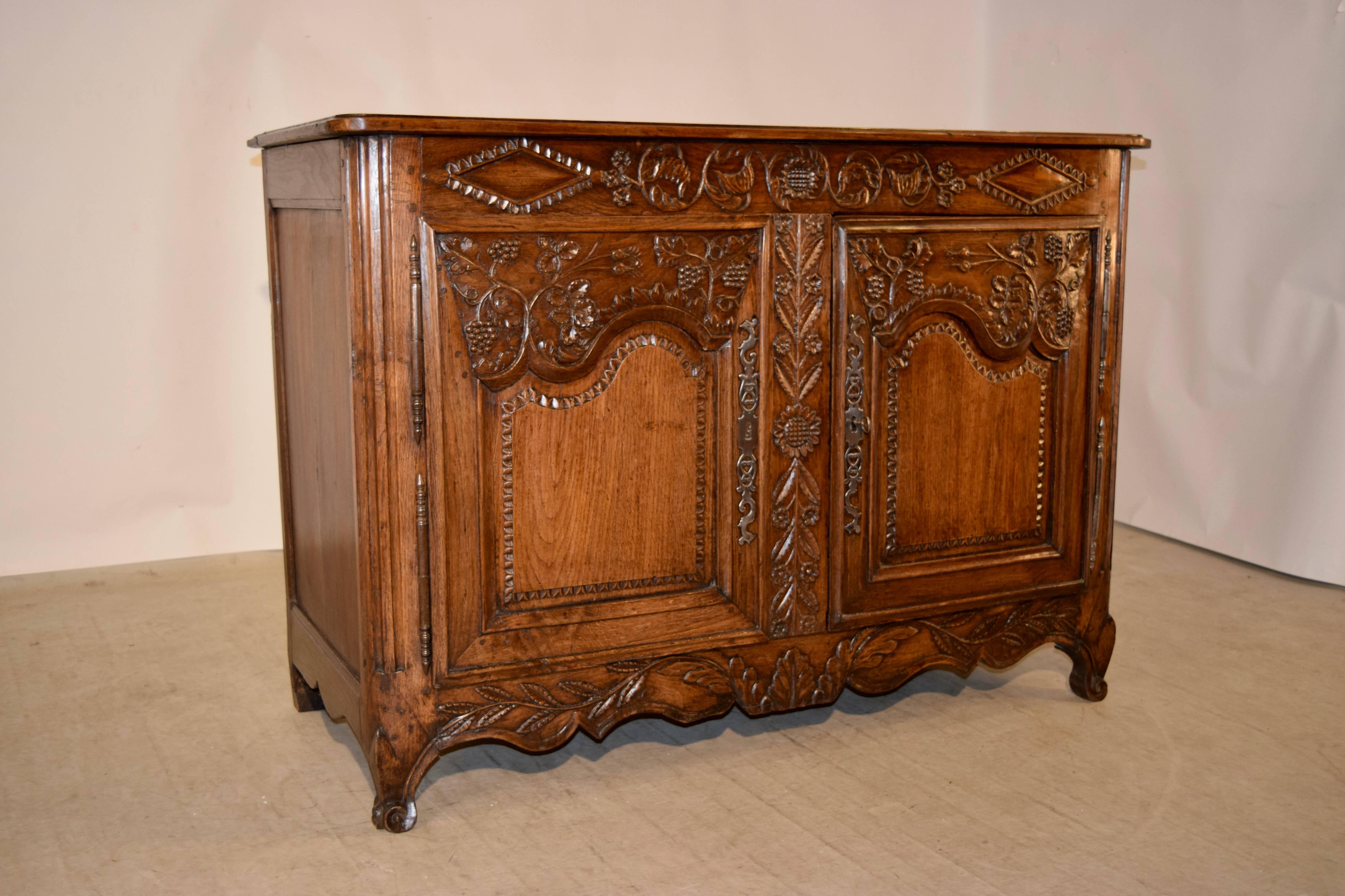 18th century French buffet made from oak. The top is banded and has a beveled edge, following down to paneled sides and a hand-carved cornice over two raised paneled and carved decorated doors which open to reveal shelving. The skirt is also