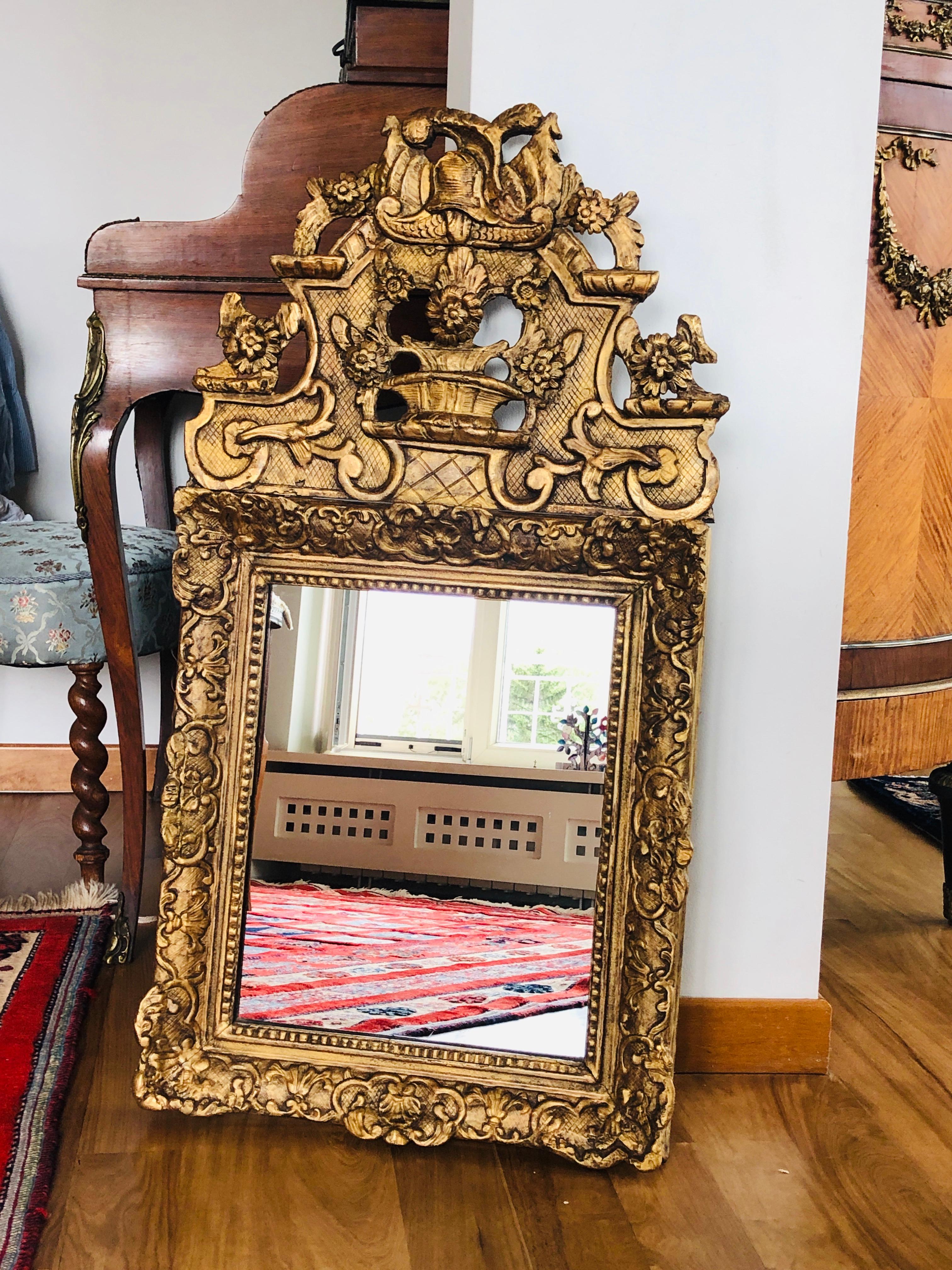 18th century carved giltwood mirror with rich ornamentation and flower basket decoration.
Very good condition after restoration.
France, circa 1770. 
 
