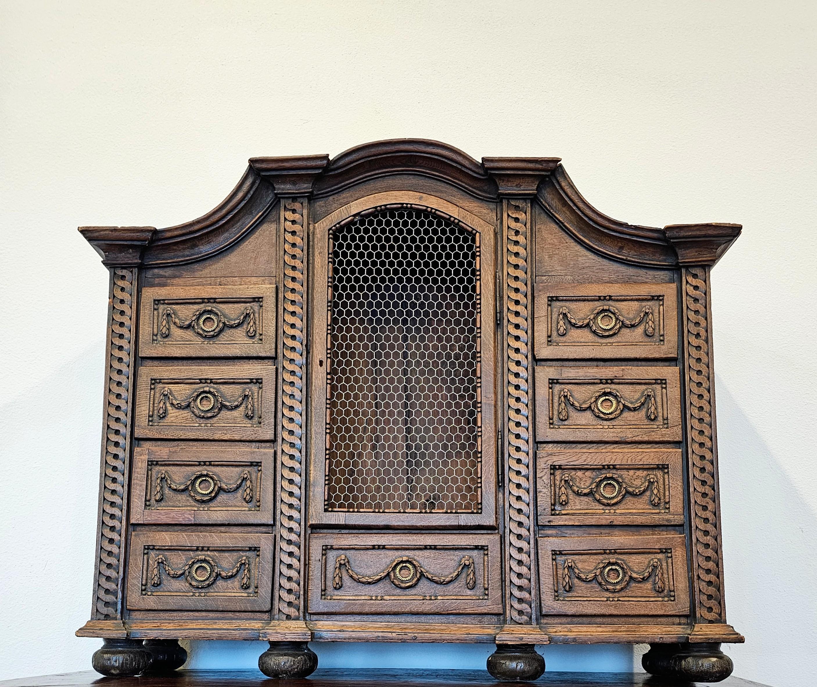 A rustic antique French Baroque carved oak tabernacle curiosity cabinet, 18th century or earlier, having an architectural form with elaborate molded cornice, over central niche, surrounded by nine drawers with hand-cut dovetail joinery, Neoclassical