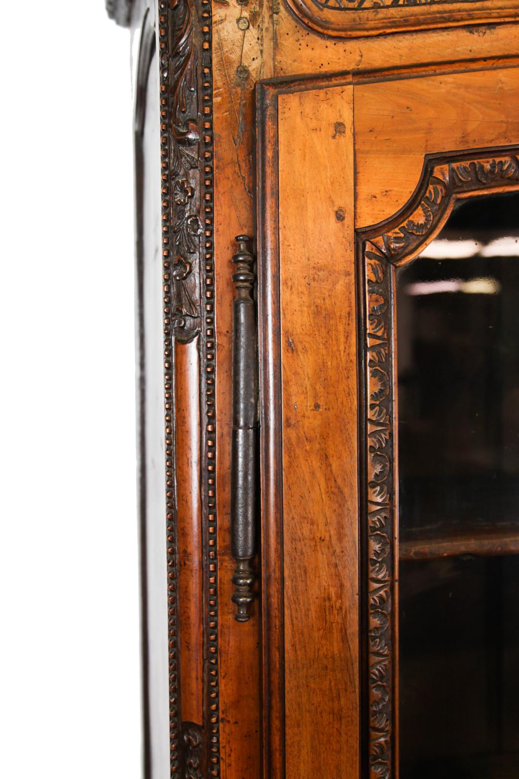18th century French carved walnut glass door cupboard, intricately carved removable cornice, carved frieze with raised molding and center cartouche with carved motif, double arched doors with original wavy glass framed with carved foliate, lower