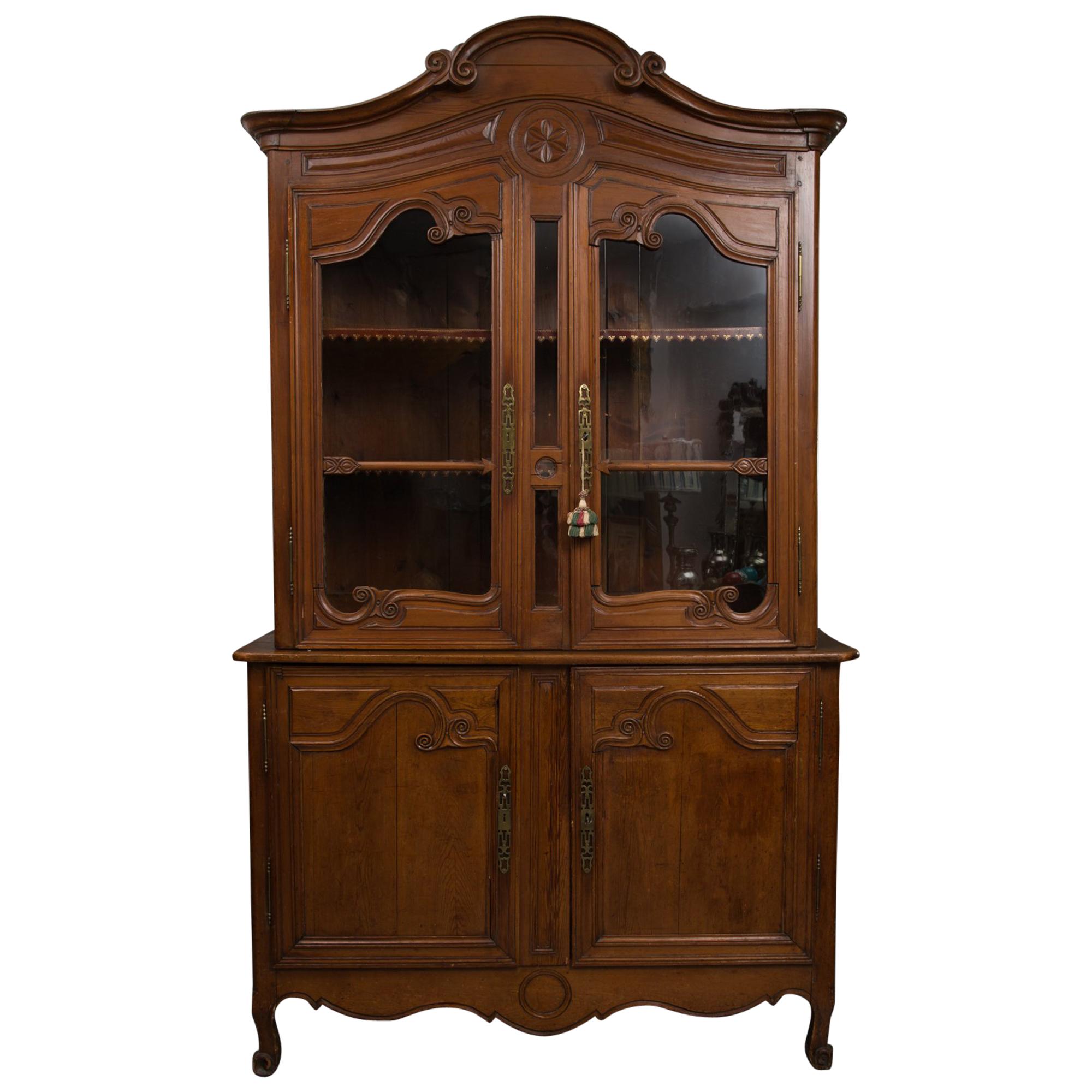This is an early French Louis XV provincial cherrywood buffet a deluxe corps with an arched cornice over a carved conforming frieze above two glazed doors situated on a bottom section with a pair of carved paneled cabinet doors over a carved, shaped