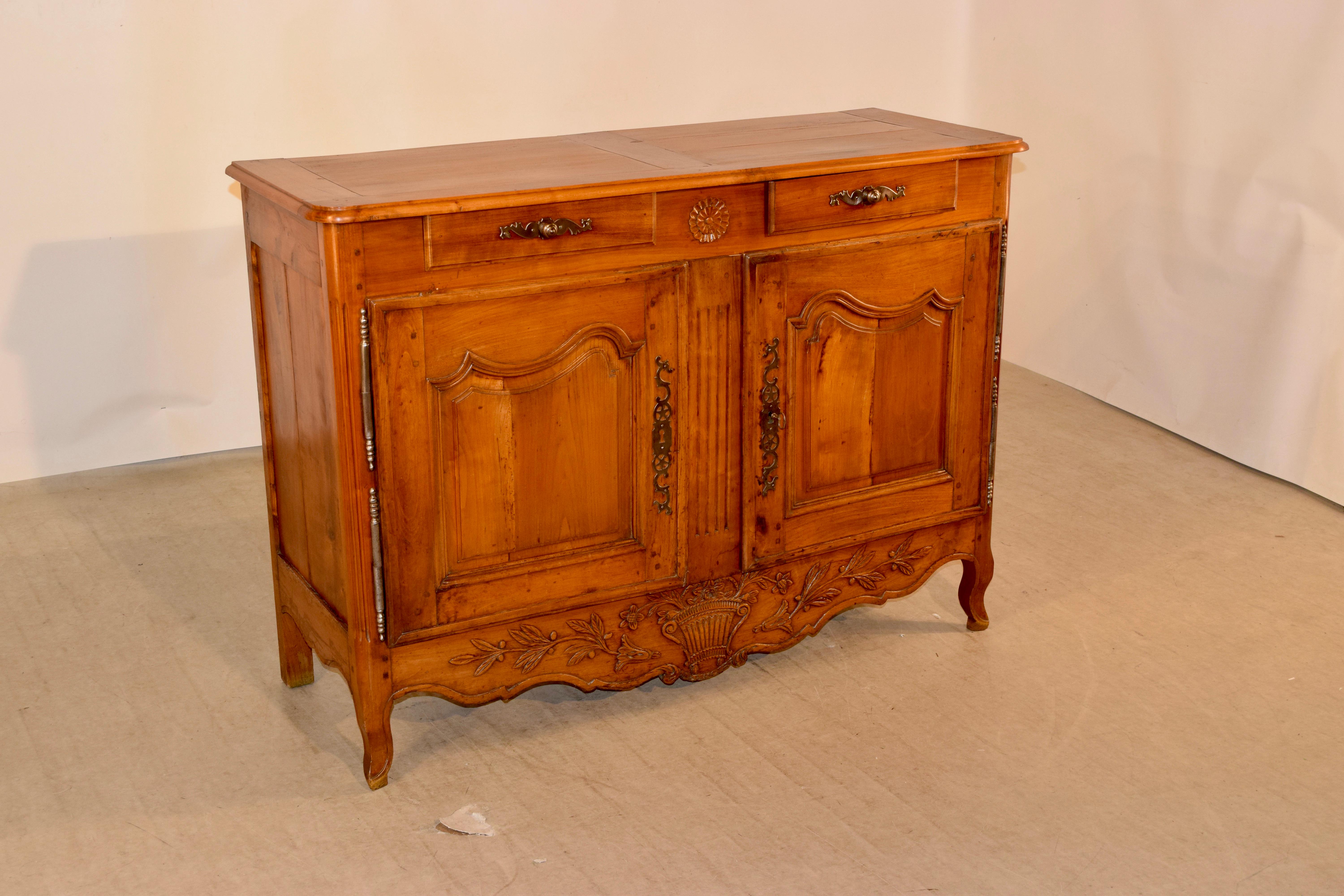 18th century cherry buffet from France. The top is banded and has a beveled edge, following down to a case with paneled sides and two drawers over two wonderfully paneled doors, which open to reveal storage. It has a lovely hand carved and scalloped