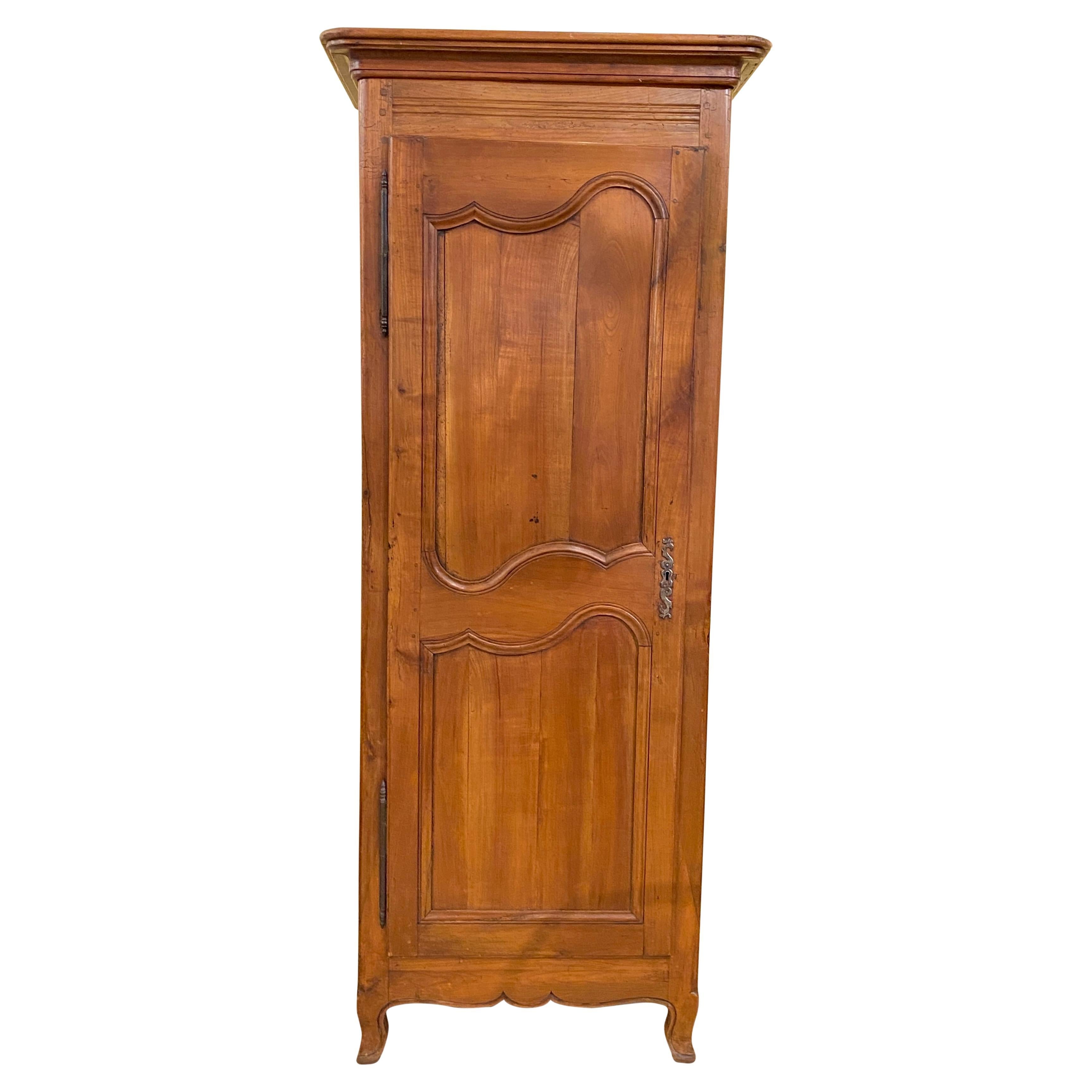This lovely antique bonnetiere, made of cherry wood with varying tones and textures, was carved and constructed in 18th century France, circa 1750. This cabinet features a single tall door with adjustable interior shelves. The door is decorated with