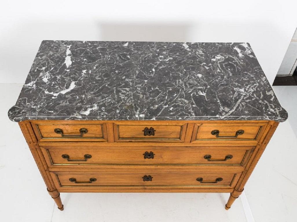 French chest of drawers with grey marble top and metal trim, circa 18th century. The piece also features two large drawers, three smaller top drawers, and decorative brass escutcheon in the shape of a ribbon bow. Please note of wear consistent with