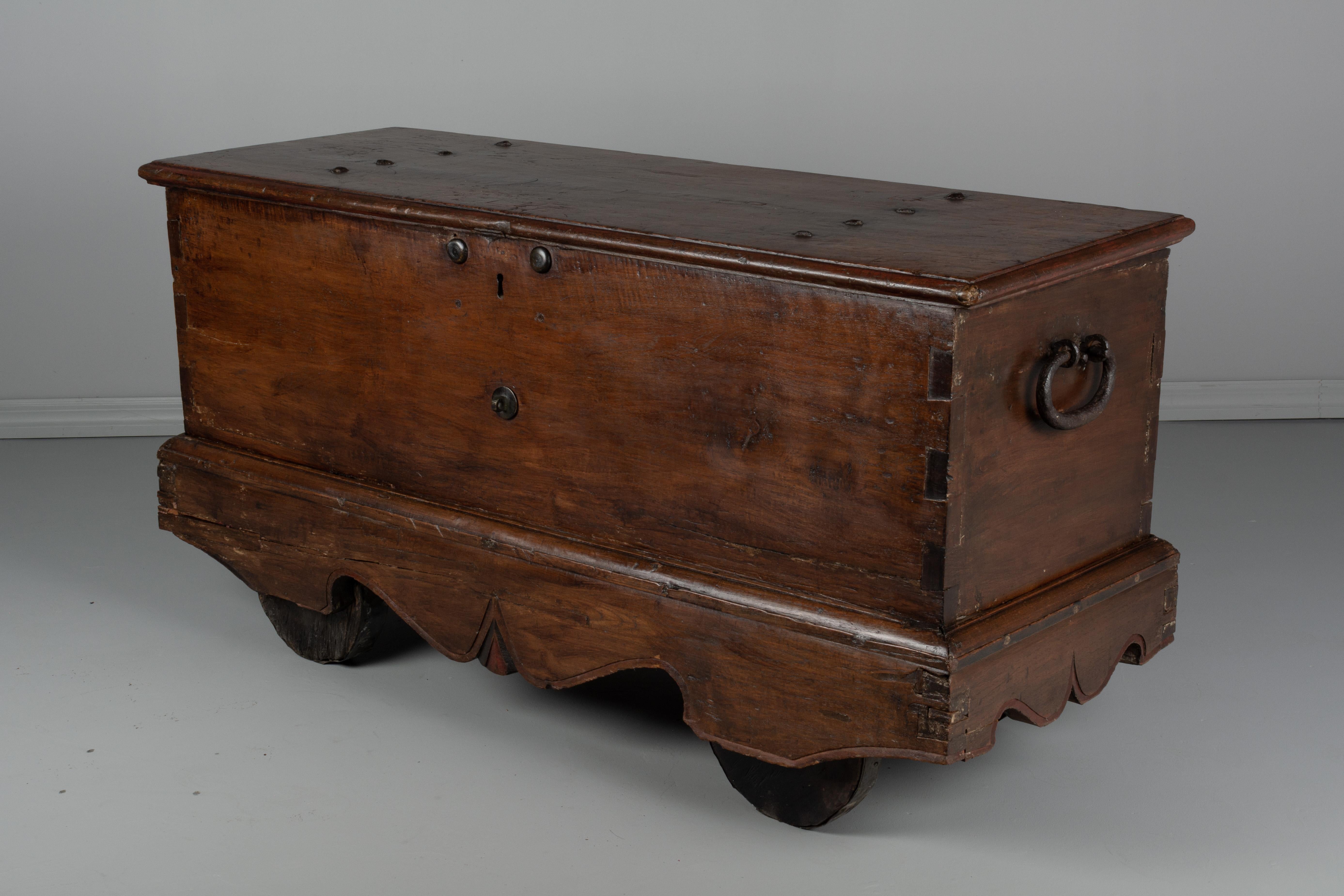 An early 18th century French coffer, or large trunk, made of solid planks of chestnut with dovetailed construction. Simple carved apron with remnants of red and black painted accents. Retains the original wooden wheels banded in metal. Large heavy