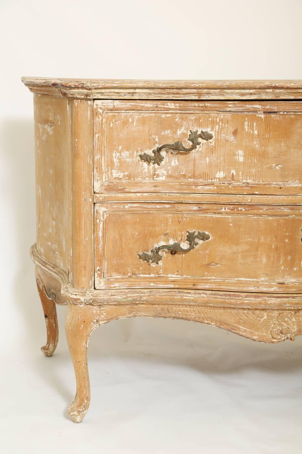 Commodo, in pino, con finitura originale, piano sagomato e modellato su base conforme, due cassetti sovrapposti ornati da maniglie rococò e scutcheons, grembiule a serpentina centrato da un cartiglio a C, sormontato da modanature, alzato su gambe a