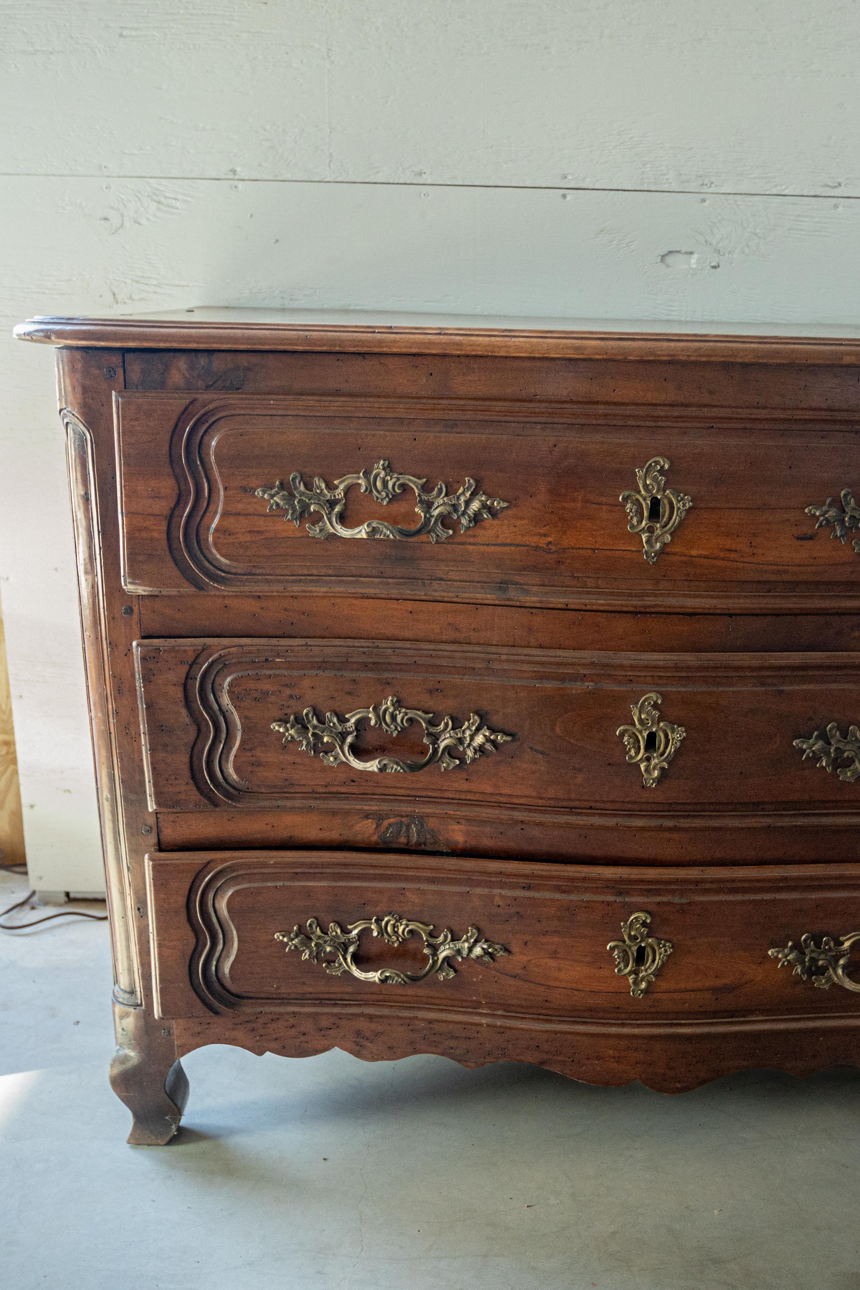 Añade un toque de elegancia y refinamiento franceses a tu hogar con esta impresionante cómoda francesa del siglo XVIII. Fabricada en estilo Luis XV, esta excepcional pieza presenta una chapa de madera bellamente labrada con una rica y cálida pátina