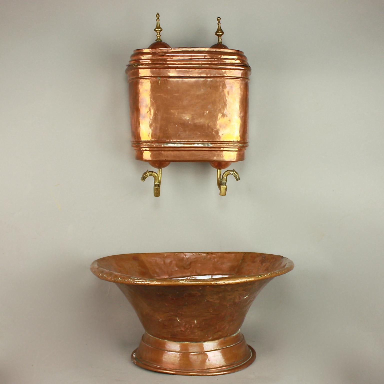 An 18th century copper repoussé fountain which was originally mounted on the wall inside the home. This Louis XVI period piece features a semicircular basin or lavabo and a fountain with lid and with its original bronze spigots and zoomorphic