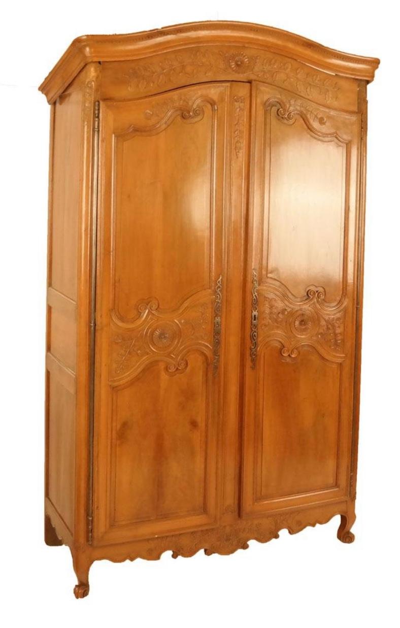 A lovely Louis XV period arched-top armoire in honey-colored cherrywood, beautifully carved with floral motifs, the two inset paneled doors retaining their original lock and hardware. The interior has been fitted with custom adjustable shelves and