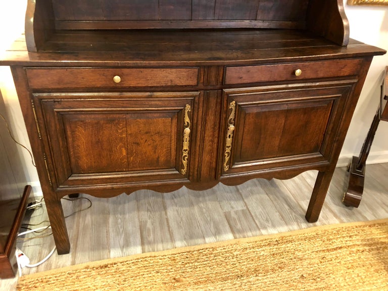 A late 18th century step-back cupboard, French Provincial Louis XV period in oak, with brass mounts and pulls, and carved wood spindles. Nice original patina.
