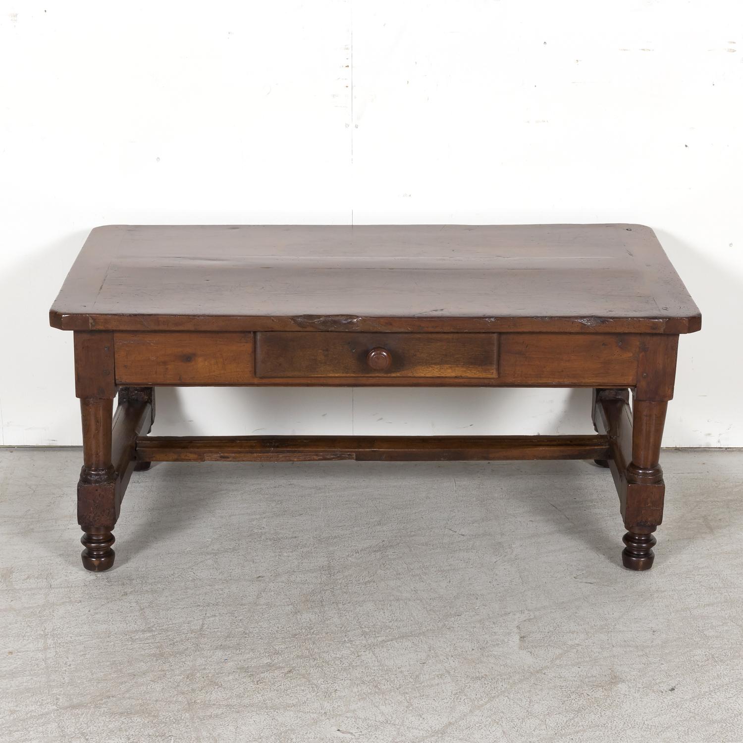 An 18th century French Country coffee table handcrafted of solid walnut in Lyon, circa 1760s, having an inset rectangular plank top with canted corners above a single center drawer with original wood knob. Raised on circular tapered legs legs ending