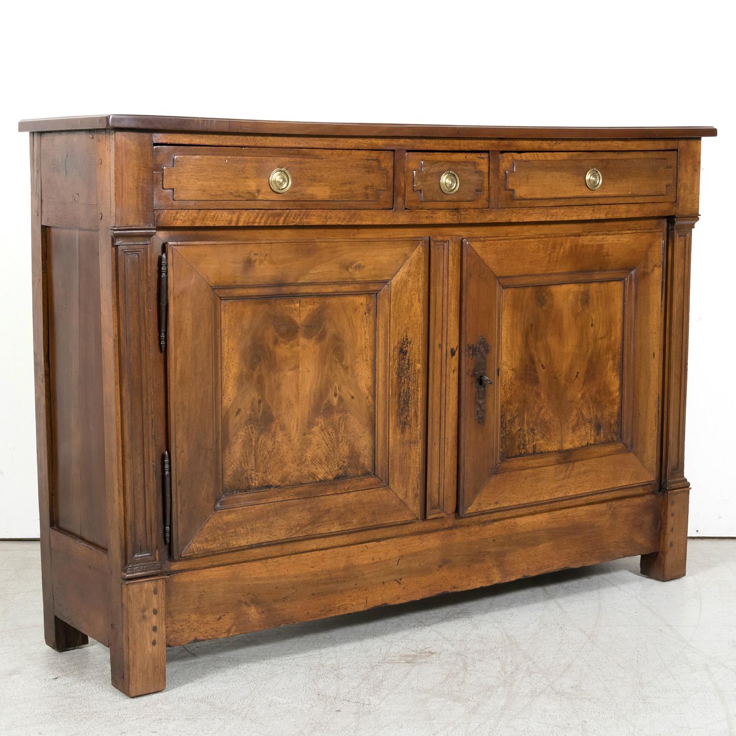 An 18th Century French Directoire period buffet handcrafted from solid walnut by talented artisans near Lyon, circa 1790s. Having a rectangular plank top that provides a great surface for serving and display above three carved drawers with brass