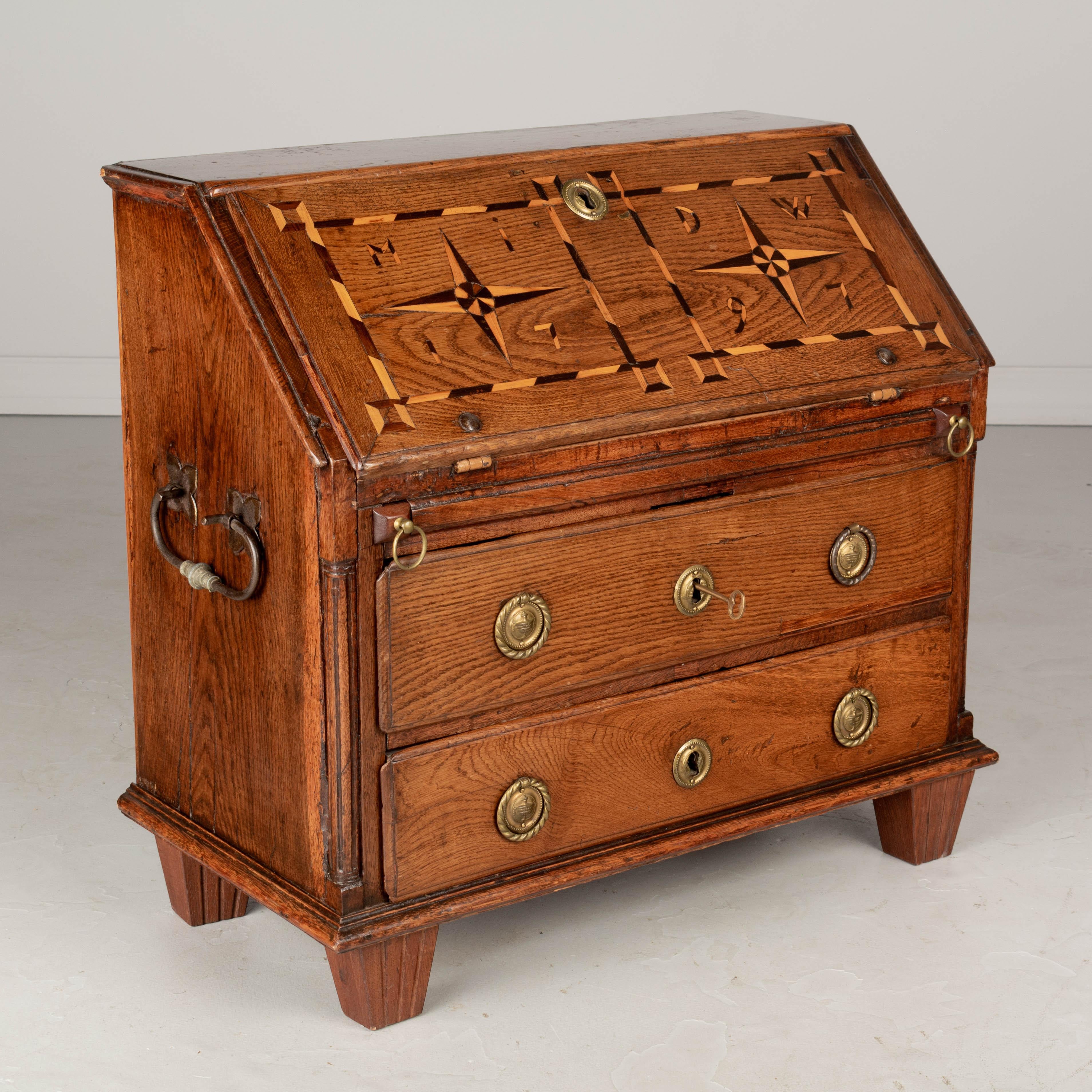 A late 18th century Country French child's Size drop front desk from Alsace. Made of solid oak with marquetry front dated 1797. Interior with seven small drawers and painted writing surface. Two dovetailed drawers with brass hardware. Large wrought