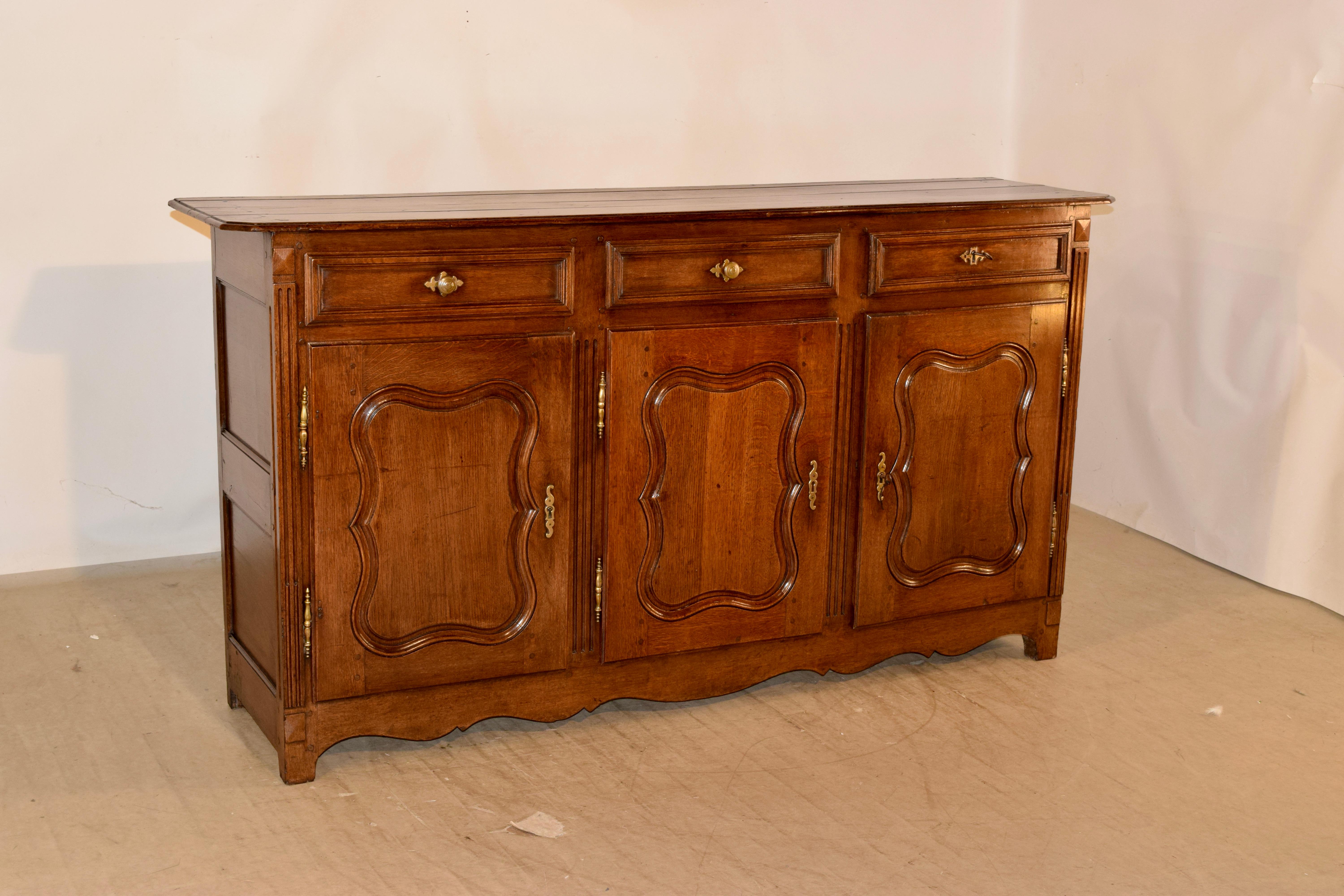 18th century oak enfilade from France with beveled edge around the top and a plate rail along the back. the sides are paneled and the front contains three paneled drawers over three raised paneled doors, which open to reveal storage. There is a