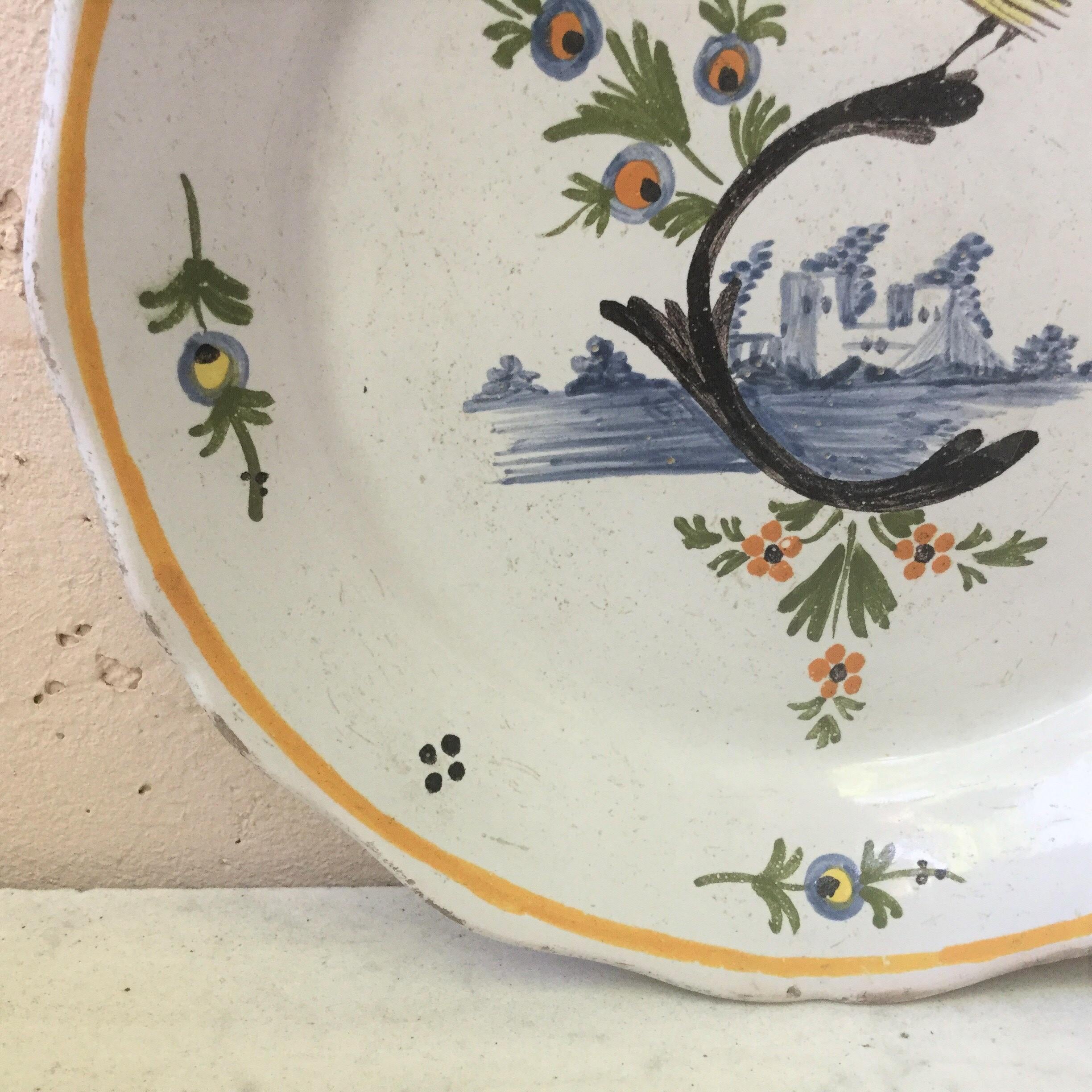 18th century French faience bird in a branch nevers plate.
A yellow bird on a branch with ruins on the back.
The border is decorated with stylized flowers.