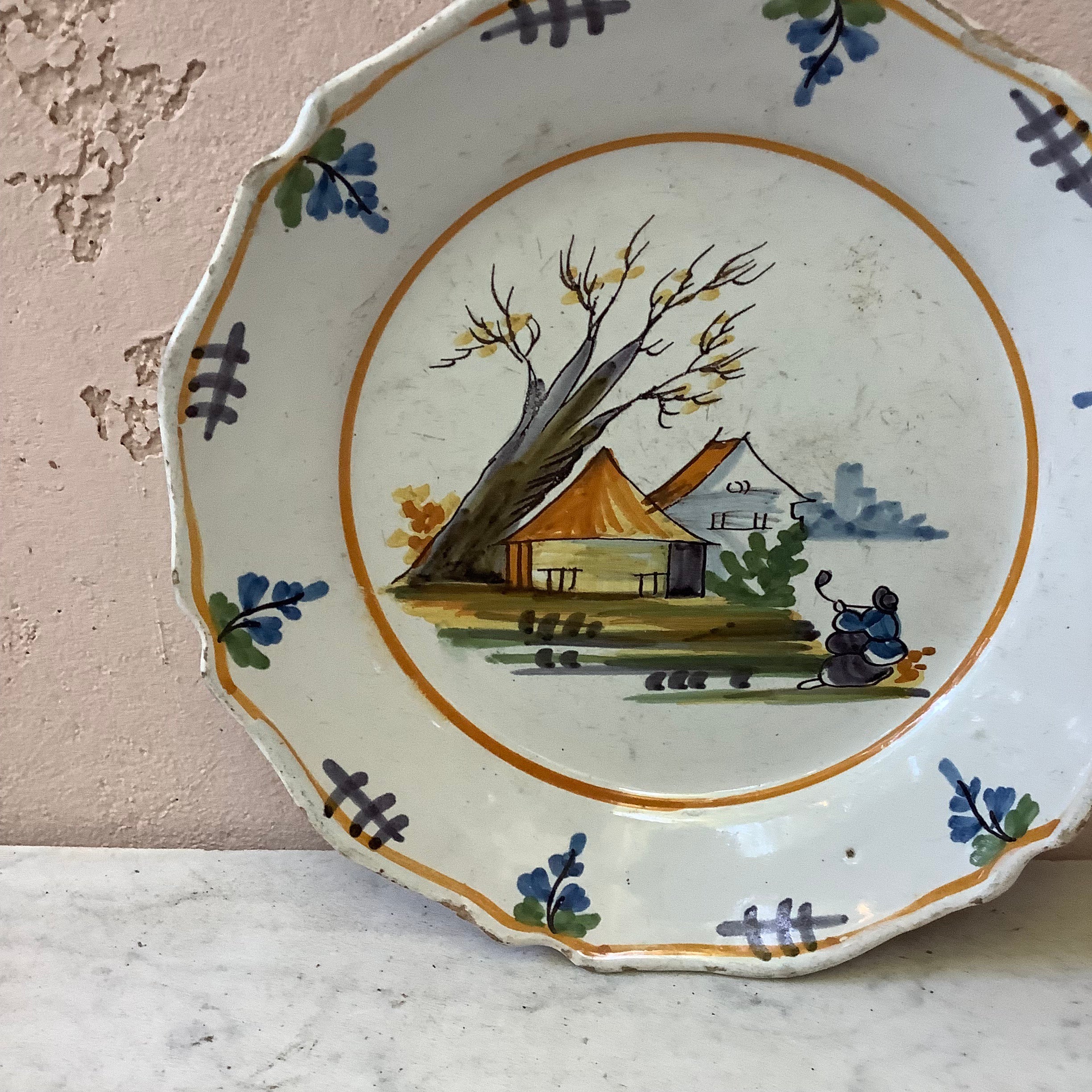 Piatto di Nevers in maiolica francese del XVIII secolo.
Case con alberi e una donna seduta.
