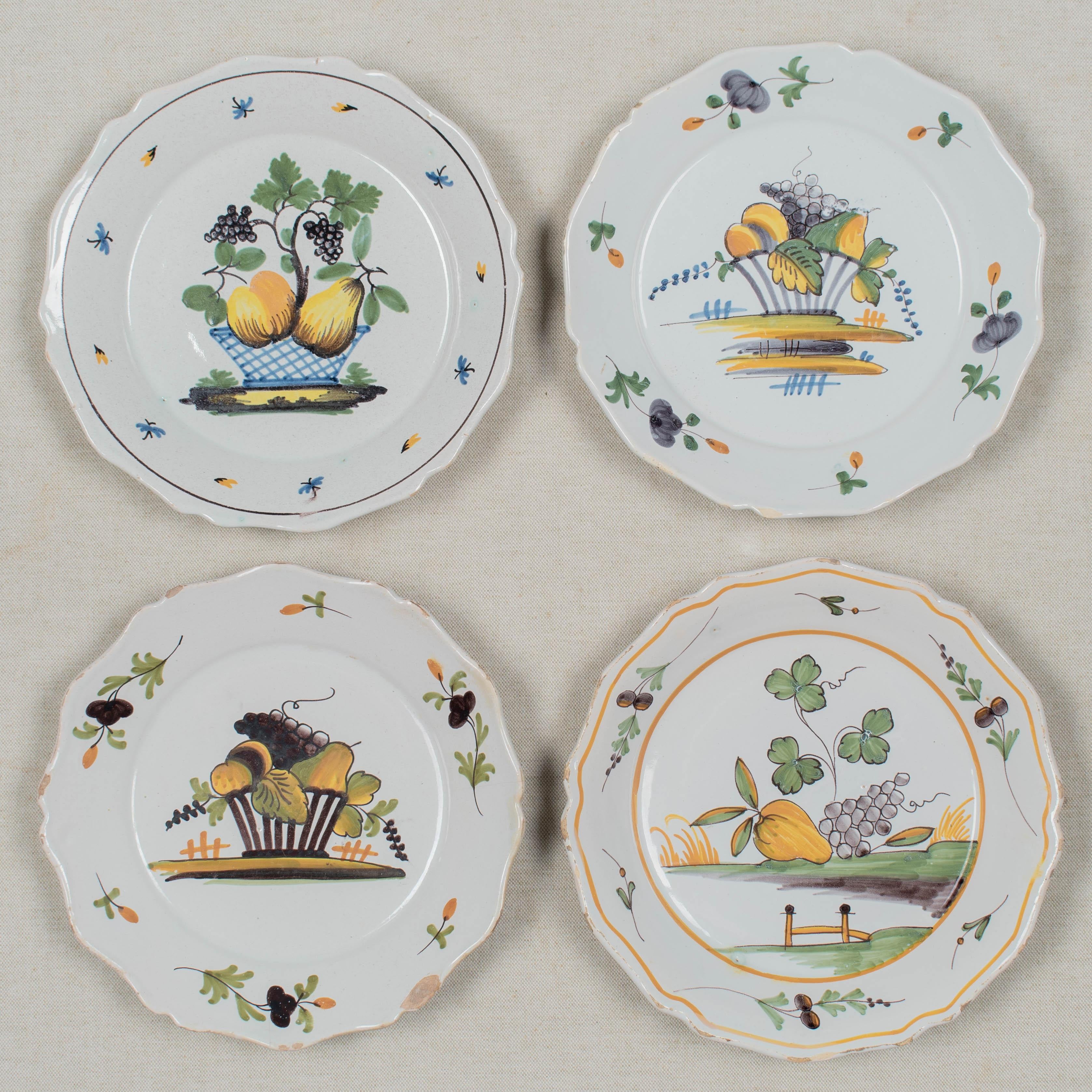 Conjunto de cuatro platos de loza francesa del siglo XVIII con decoración primitiva pintada a mano de cestas de frutas y uvas, cada uno de ellos por artistas diferentes. En estado variable, con desconchones y pérdidas de vidriado en los bordes del