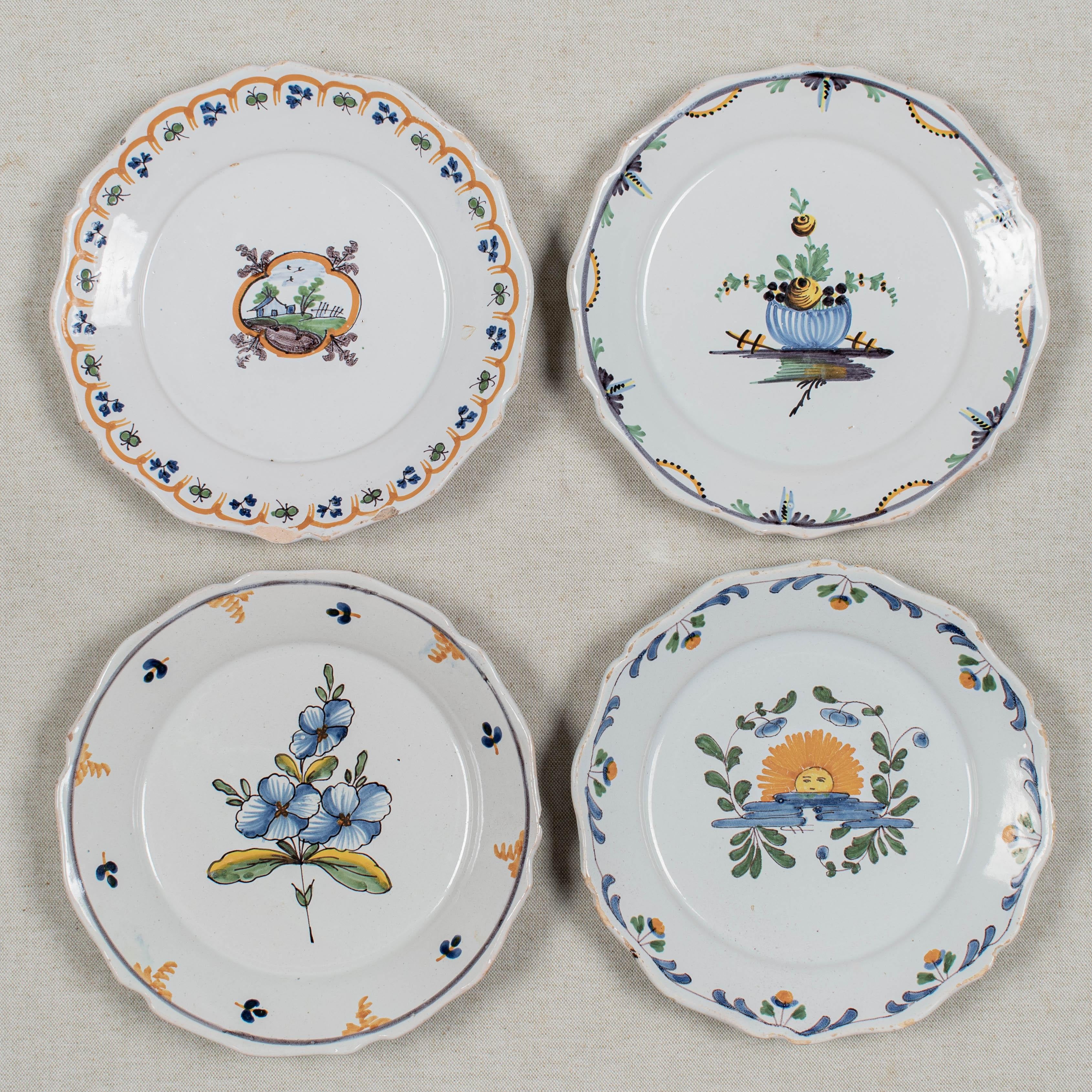 Conjunto de cuatro platos de loza francesa del siglo XVIII con decoración primitiva pintada a mano, cada uno por artistas diferentes. En estado variable, con desconchones y pérdidas de vidriado en los bordes del borde festoneado. No se observan