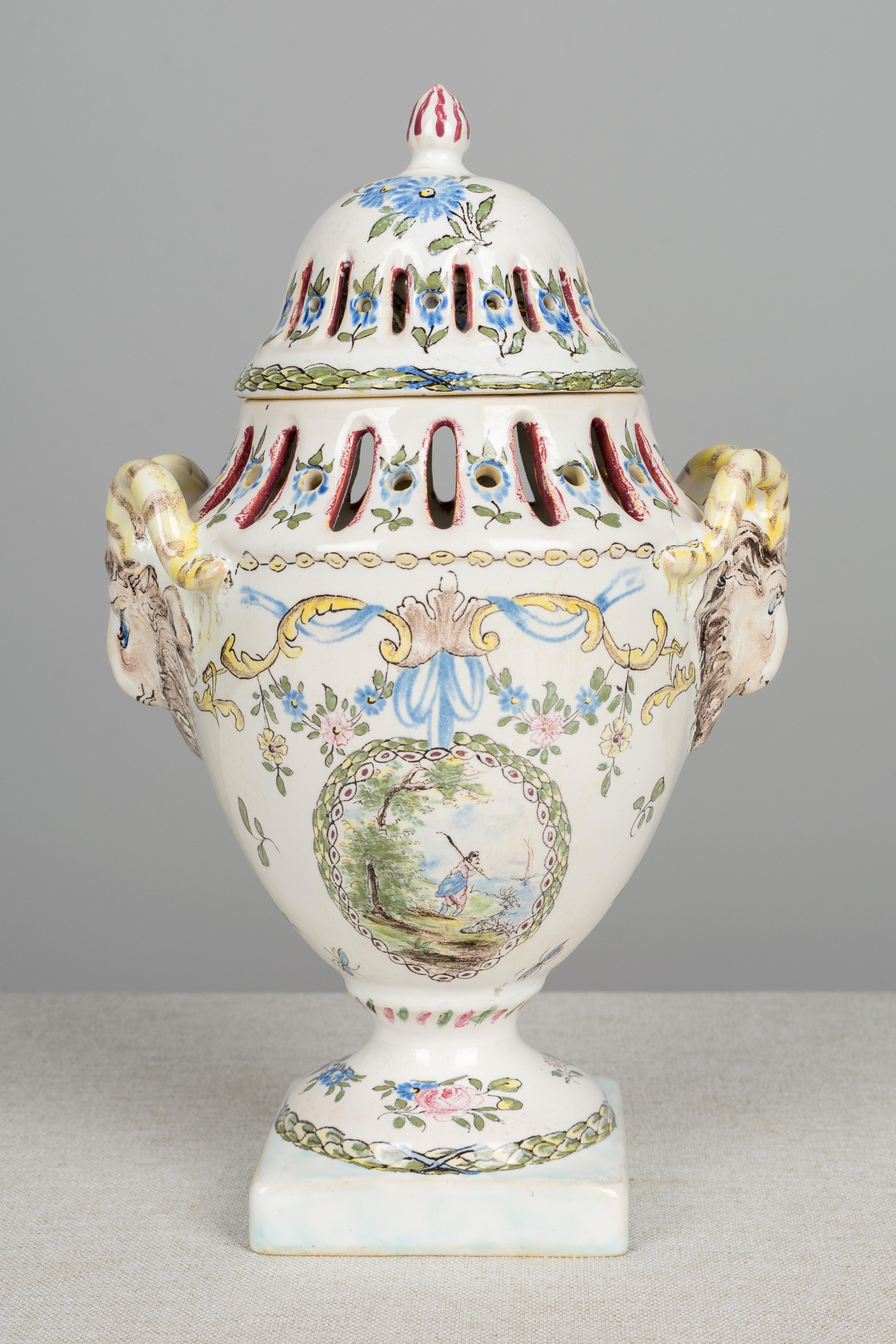 An 18th century French faience potpourri urn with a pierced fitted lid, through which scent may slowly diffuse. Lovely delicate hand painted floral decoration in pastel pink, blue, green and yellow. Whimsical sculpted ram heads form the handles. One