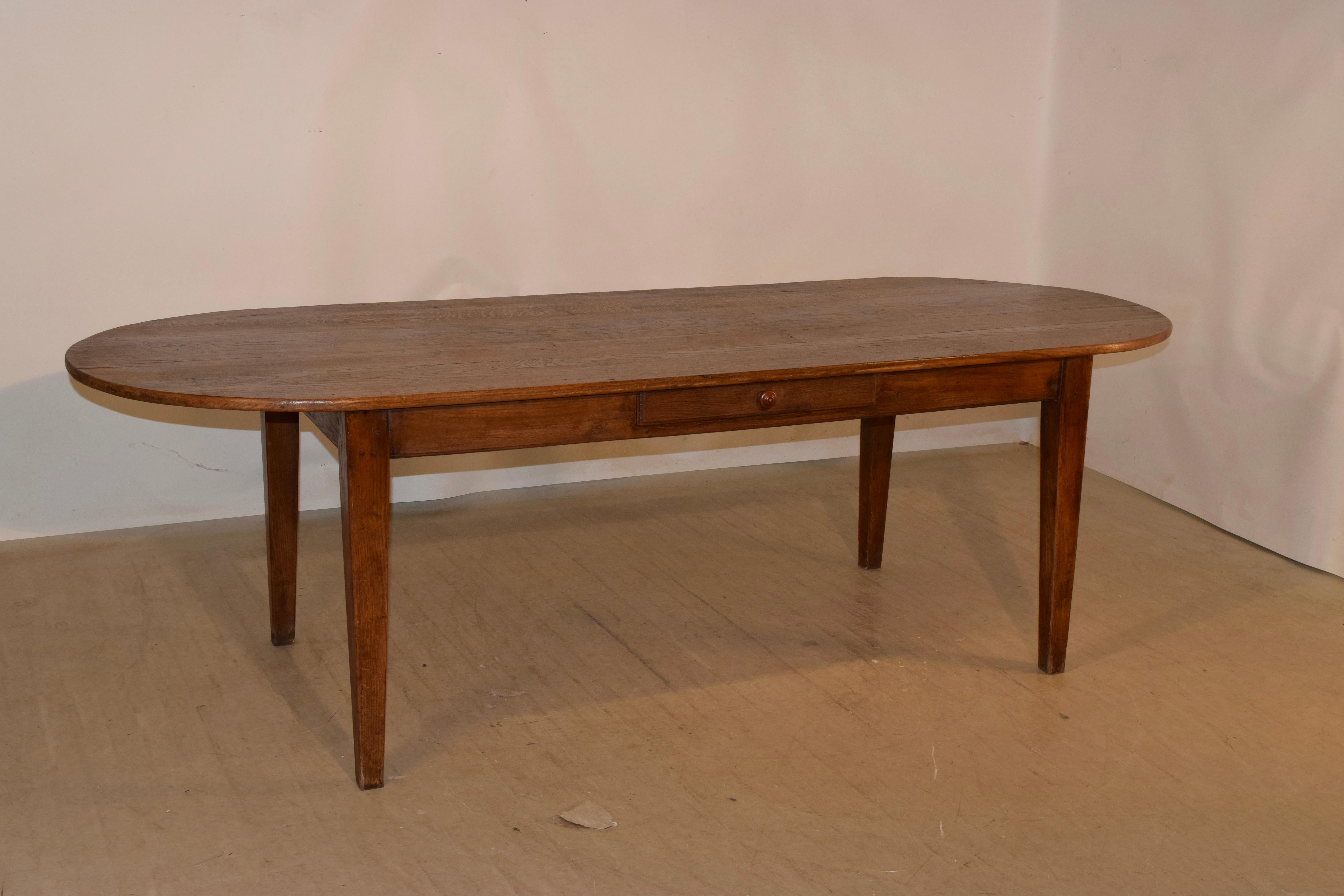 18th century chestnut farm table from France with a plank top and oval shaped ends, following down to a simple apron, which contains a single drawer, over tapered legs. The apron measures 24 inches in height.