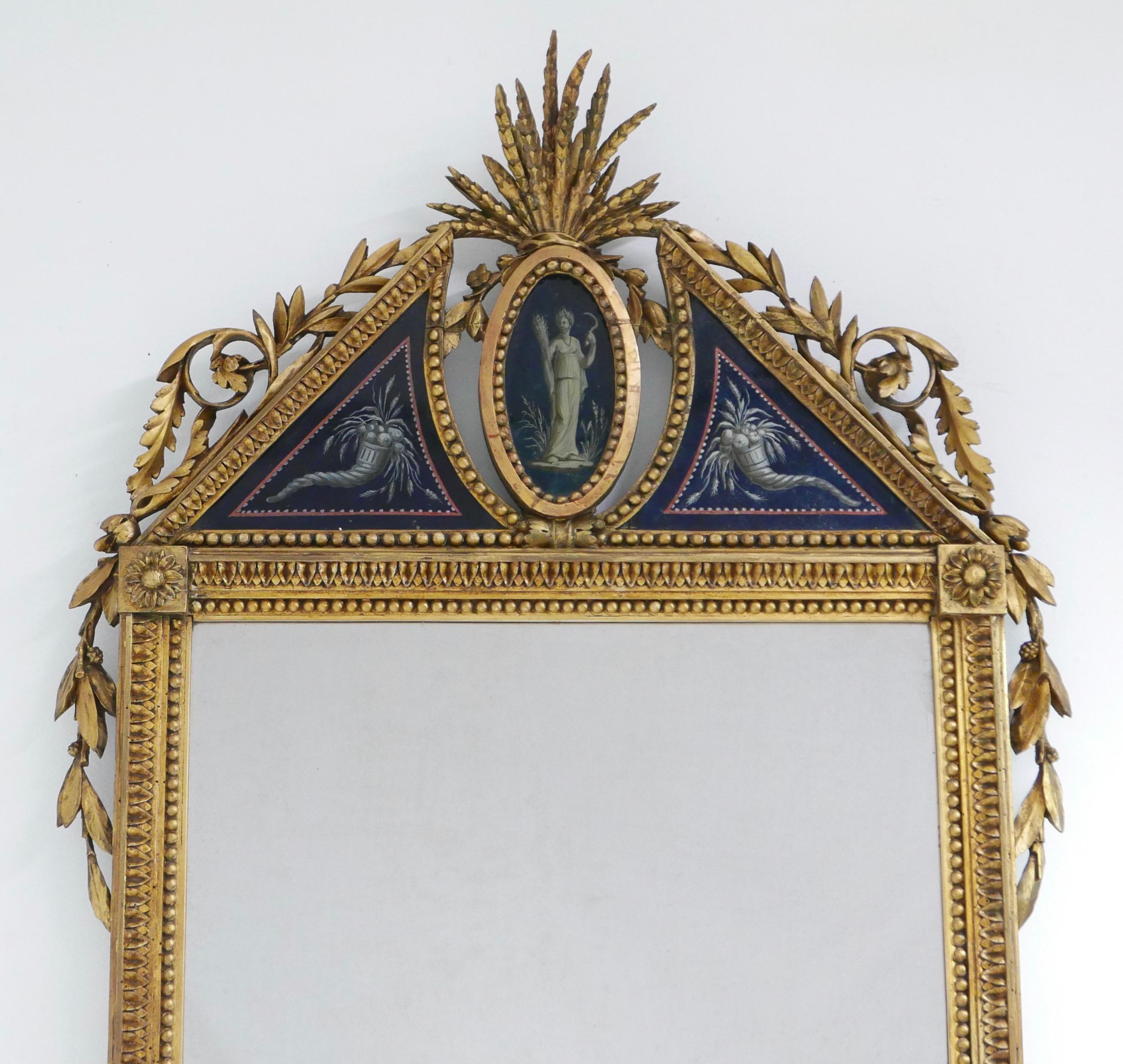 Ein prächtiger, kunstvoll geschnitzter und vergoldeter Spiegel mit einer Krone aus églomisé (rückseitig bemaltes Glas), die die griechische Göttin Demeter darstellt, flankiert von einem Paar Füllhörner.
Demeter ist die Göttin der Fruchtbarkeit, des