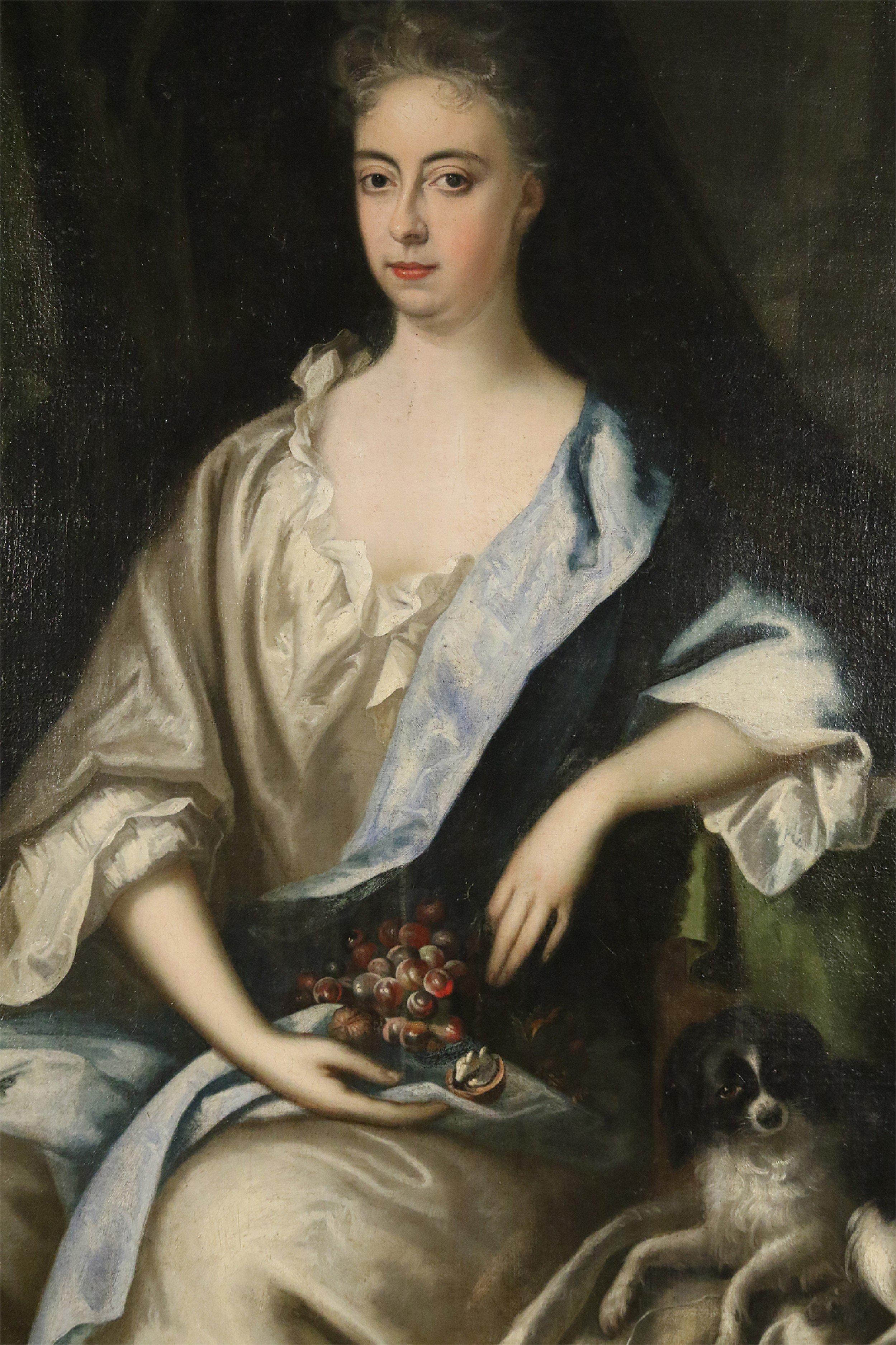 Peinture à l'huile française (18e siècle) représentant une femme tenant des raisins, assise à côté d'un chien, dans un cadre rectangulaire en bois sculpté et doré.