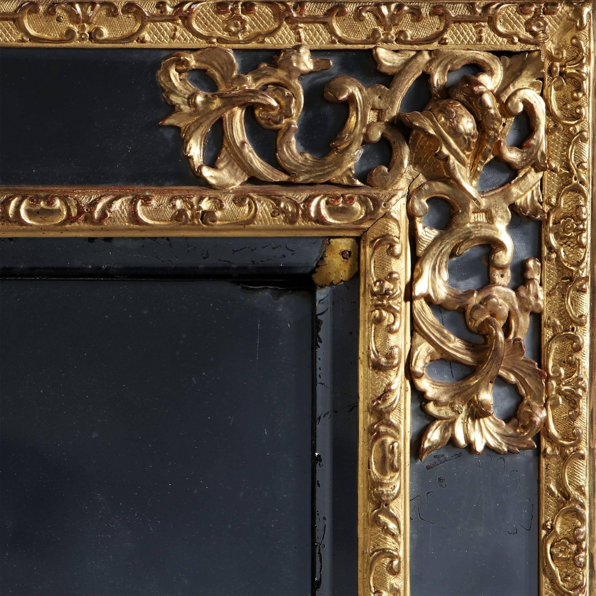 A late 18th century French giltwood mirror, the central bevelled mercury plate surrounded by carved C scrolls and trellis work border, flanked by a marginal mirror, with pierced corner mounts of a classical helmet and scrolling foliage.