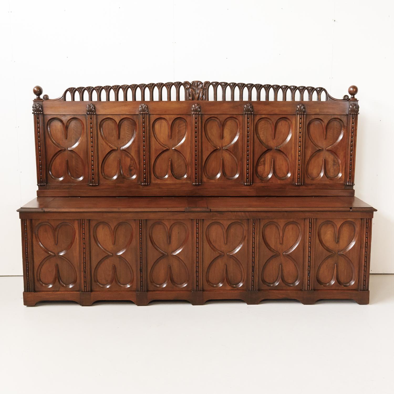 18th century French Gothic Revival period chateau settle with double lift seat handcrafted of solid old growth French walnut by talented artisans in Lyon, circa 1760s. This intricately carved hall bench features six high relief hand carved panels on