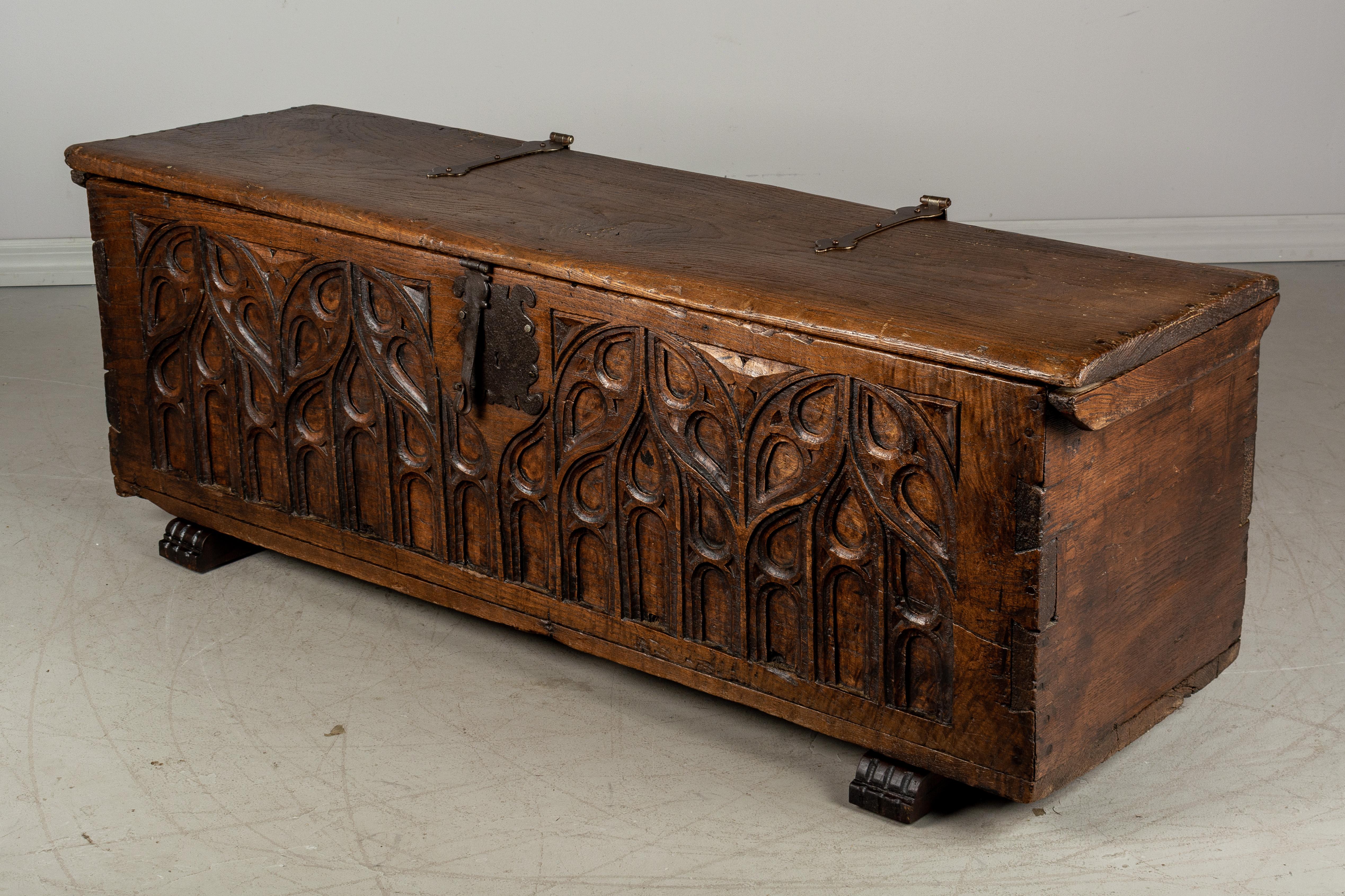 An early 18th French Gothic style blanket chest or bench made of solid chestnut with hand carved architectural relief across the front. Thick wood planks are joined using miter and dovetailed construction. Wood has beautiful character with waxed