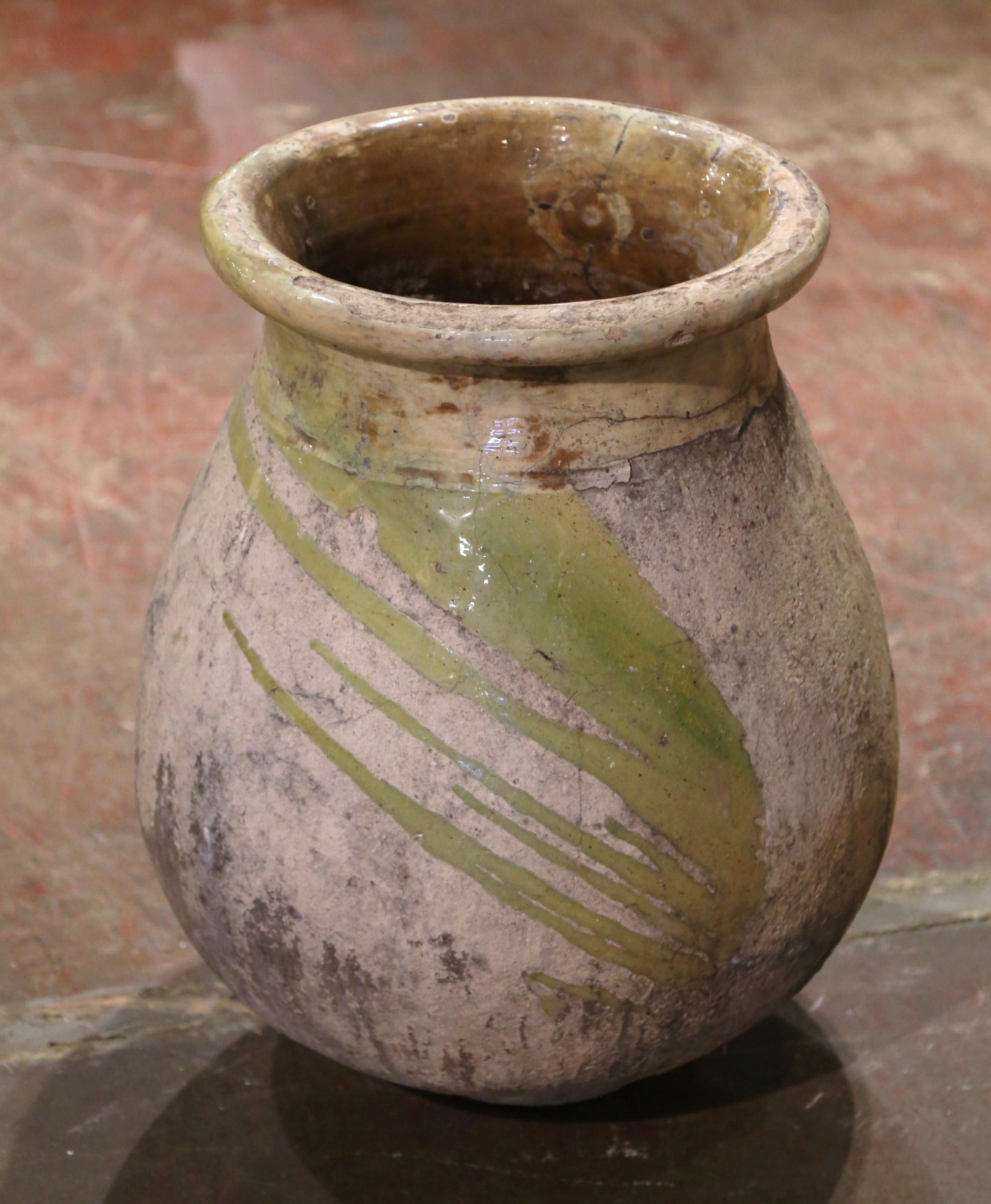 This antique earthenware olive jar was created in Biot, Southern France, circa 1760. Made of blond clay and neutral in color, the terracotta vase has a traditional round bulbous shape. The rustic, time-worn pot features a pale green glaze around the