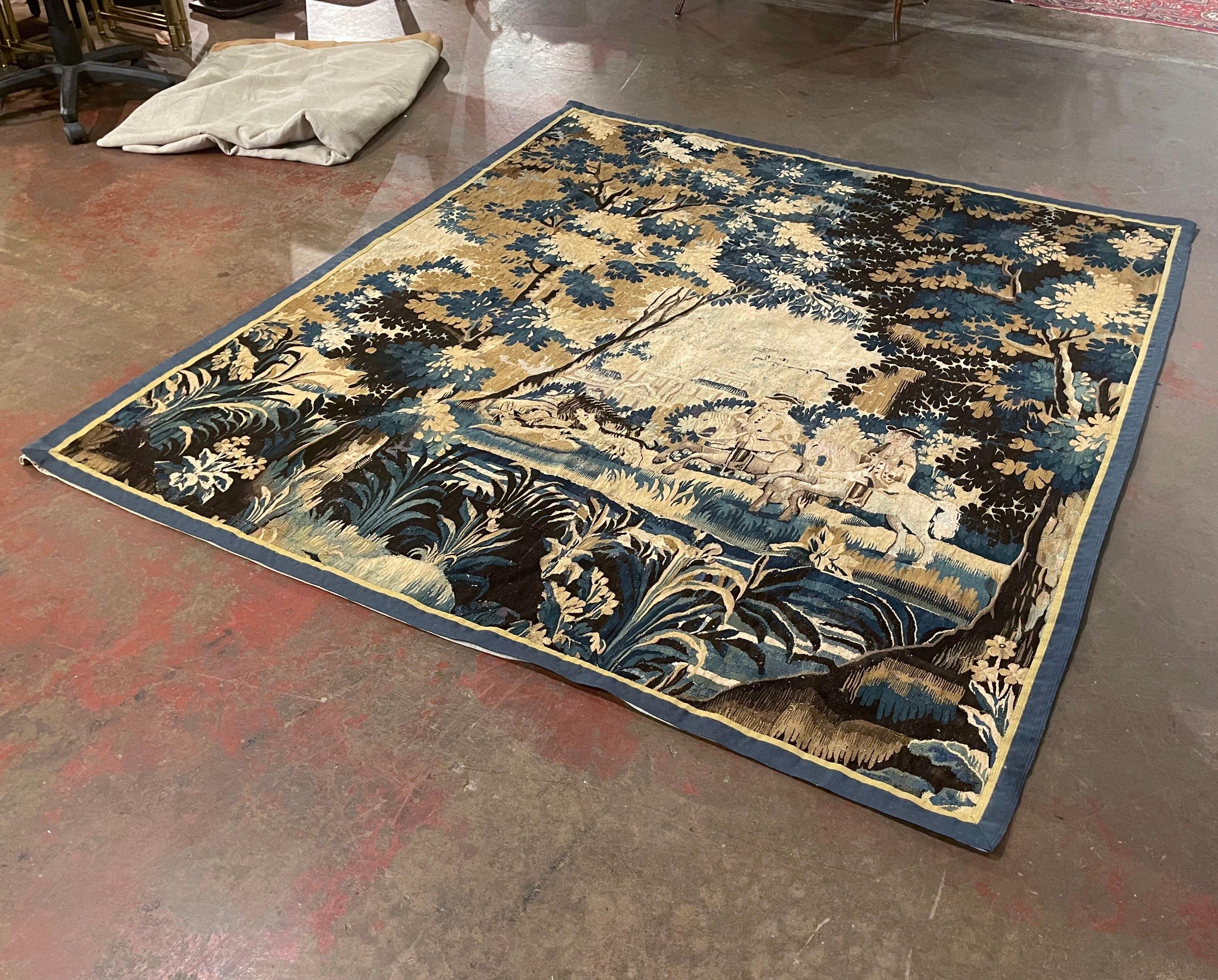 This antique tapestry was woven in Aubusson, France, circa 1760. Almost square in shape, the colorful wall decor depicts a hunting scene with a two noblemen on horseback chasing a wild boar with two dogs, embellished with trees, foliage, and a