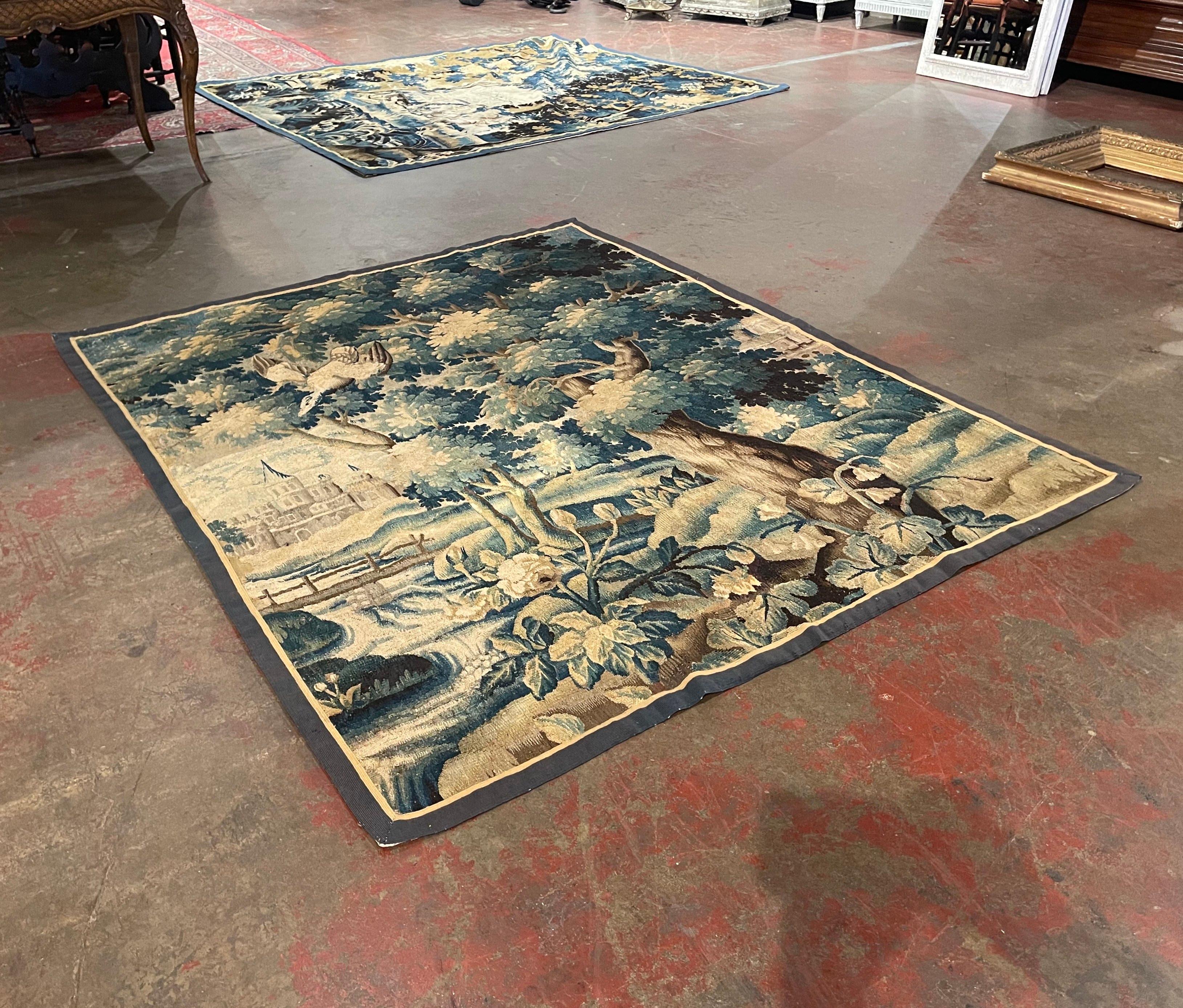 This antique tapestry was handwoven in Aubusson, France, circa 1760. Rectangular in shape, the colorful wall decor depicts a wooded landscape scene with a large, mature tree in the foreground, with a stream, a small bridge, and two castles in the