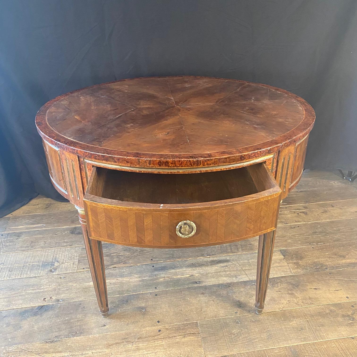  
Elegante table française du XVIIIe siècle légèrement ovale à quatre pieds fuselés cannelés et deux tiroirs, finement plaquée de noyer et de merisier. Le plateau de la table est orné d'une belle incrustation centrale qui rehausse son design. La