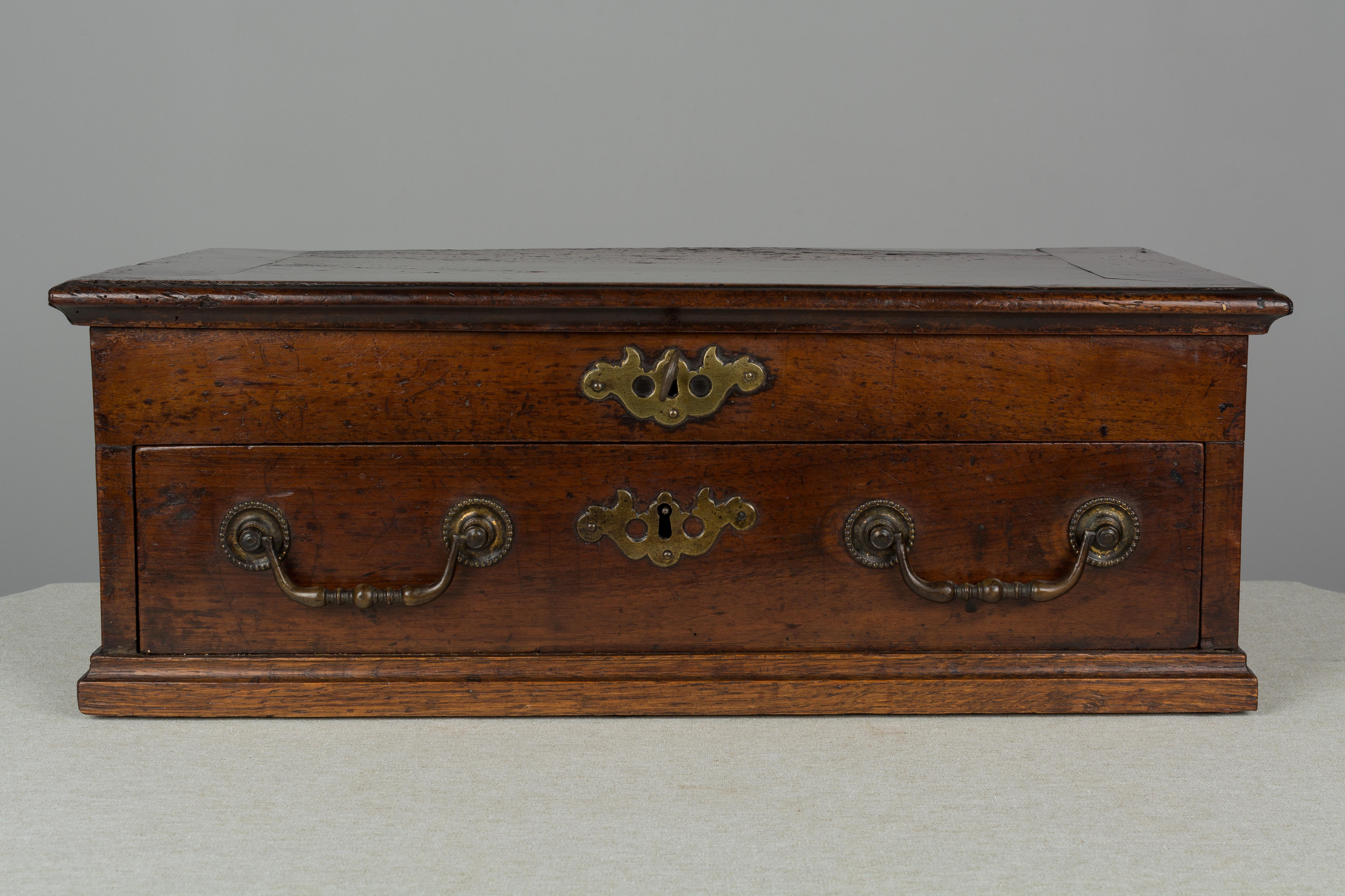 An 18th century French walnut box with a dovetailed drawer and hinged lid, opening to a divided interior with two small removable compartments. Original brass hardware with working lock and new key. Original paper label affixed to the inside of lid