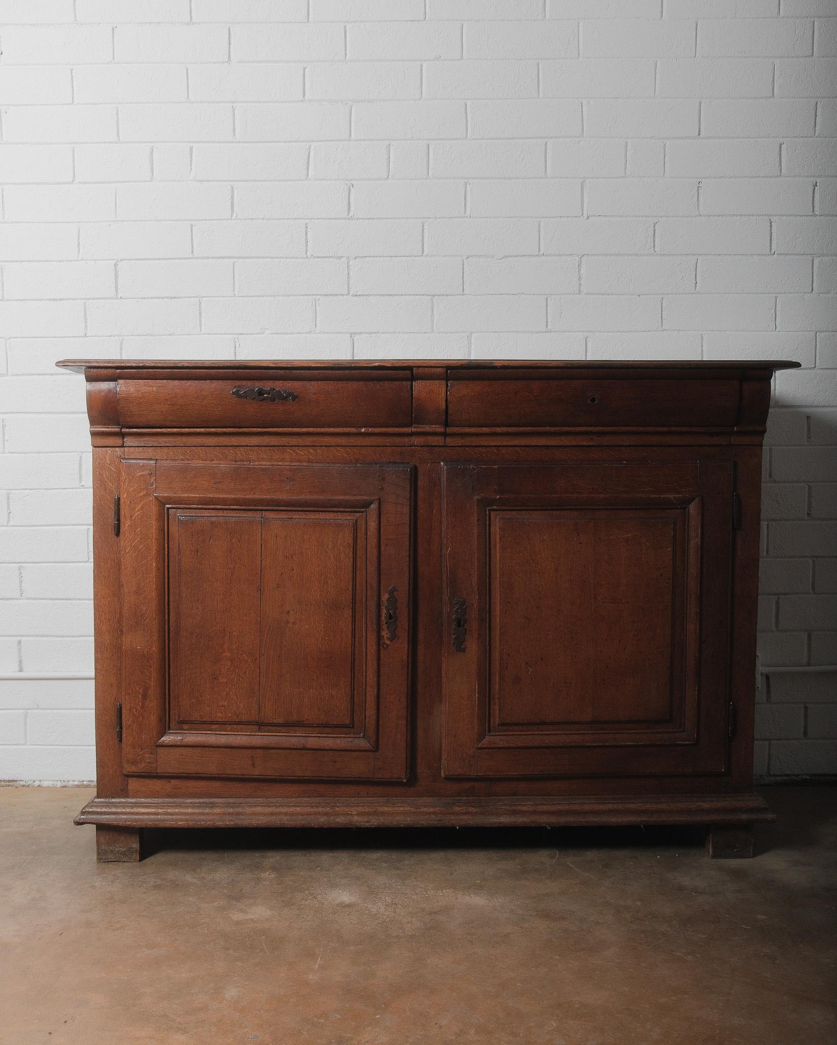 This striking 18th-century French Louis XIII provincial buffet is a testament to the enduring beauty of early French craftsmanship. Made from solid oak, it features robust, linear construction with deeply paneled doors, hand-carved moldings, and a