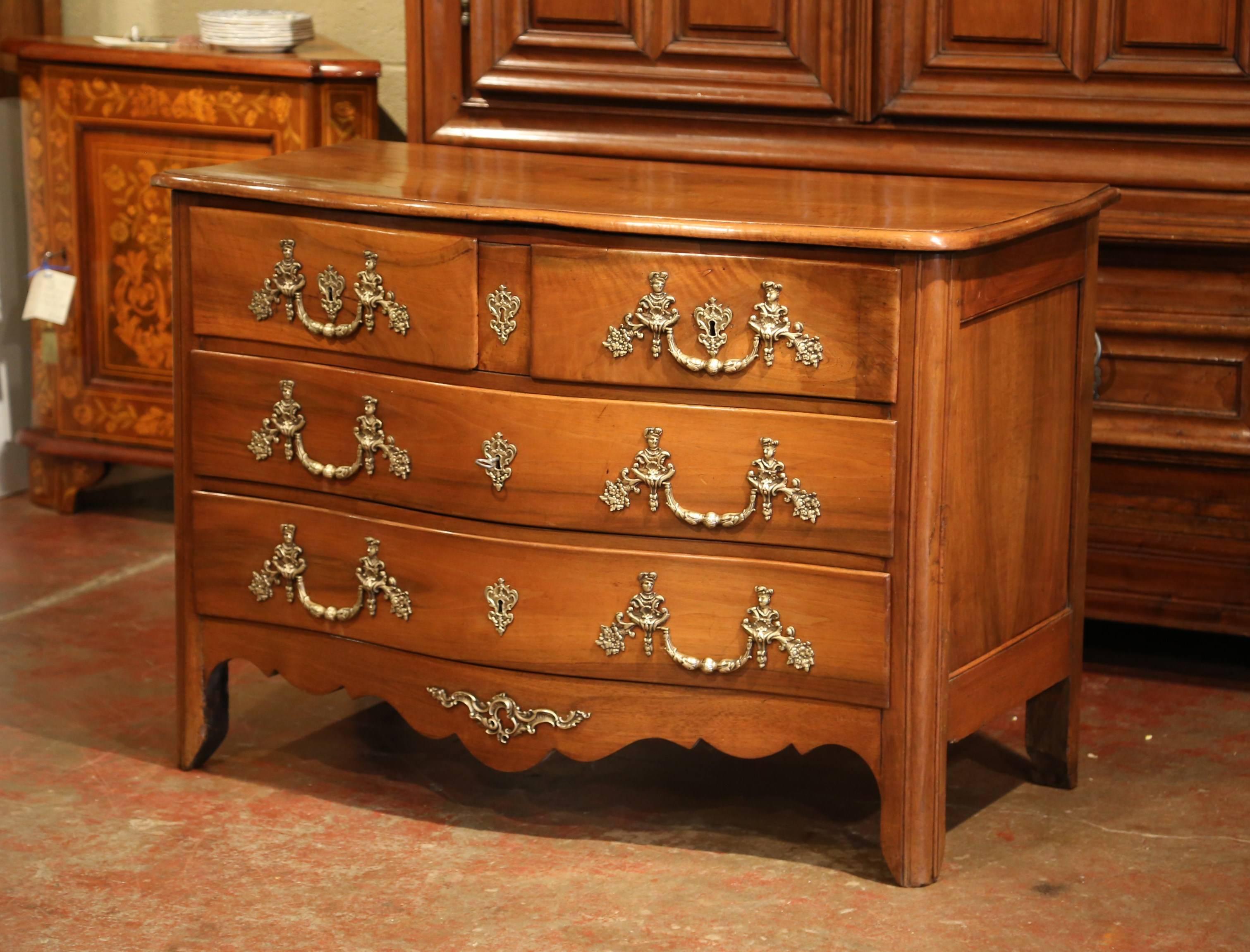 This traditional, antique chest of drawers was crafted in the Poitou region of France, circa 1800. The fruit wood commode stands on curved feet over a scalloped apron decorated with a center bronze mount; it features four serpentine drawers across