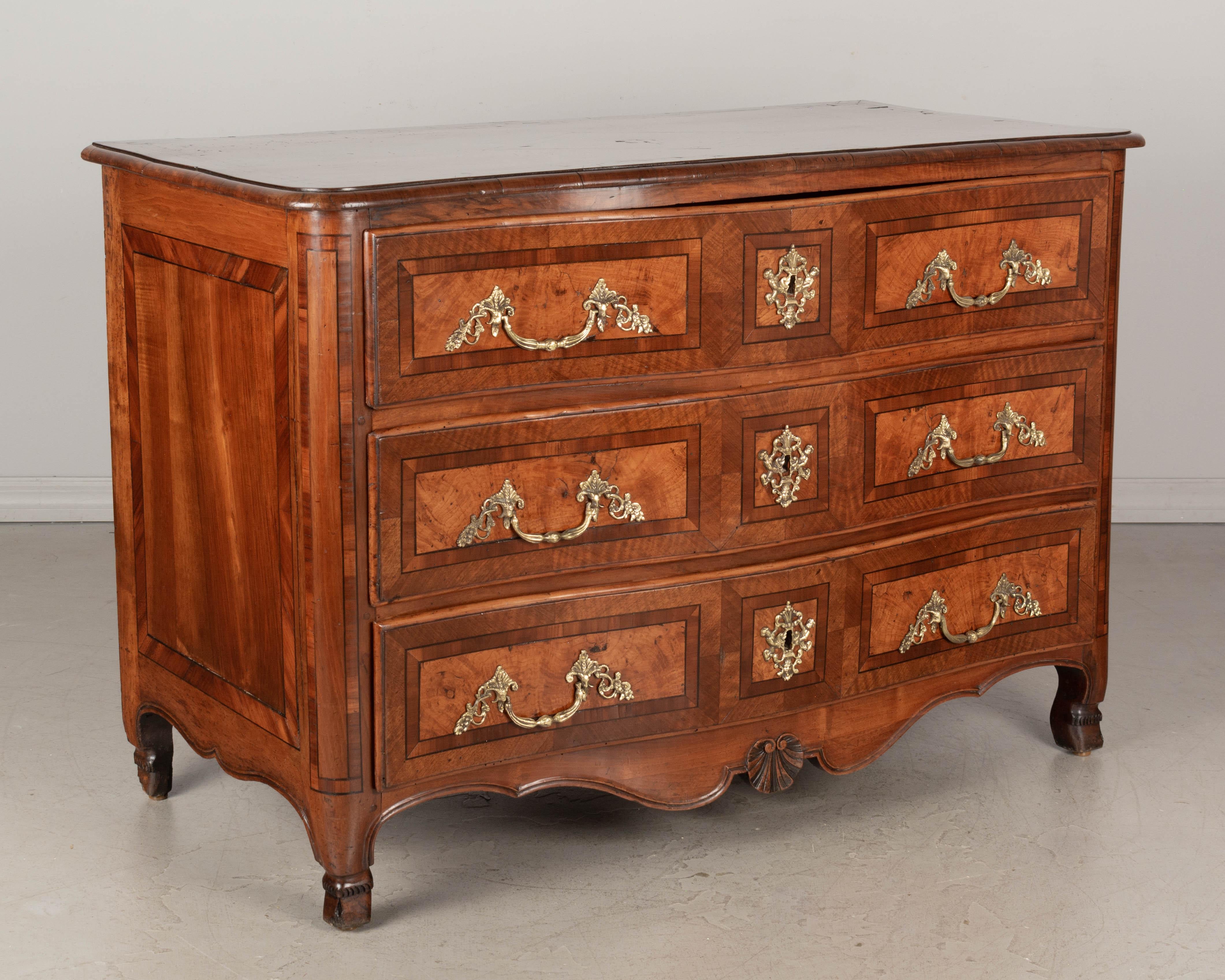 An 18th century French Louis XIV style commode from Grenoble with fine marquetry inlay of cherry, walnut and mahogany. Three dovetailed drawers with slightly serpentine front. Top has rounded front corners and a rosebud inlaid in the center.