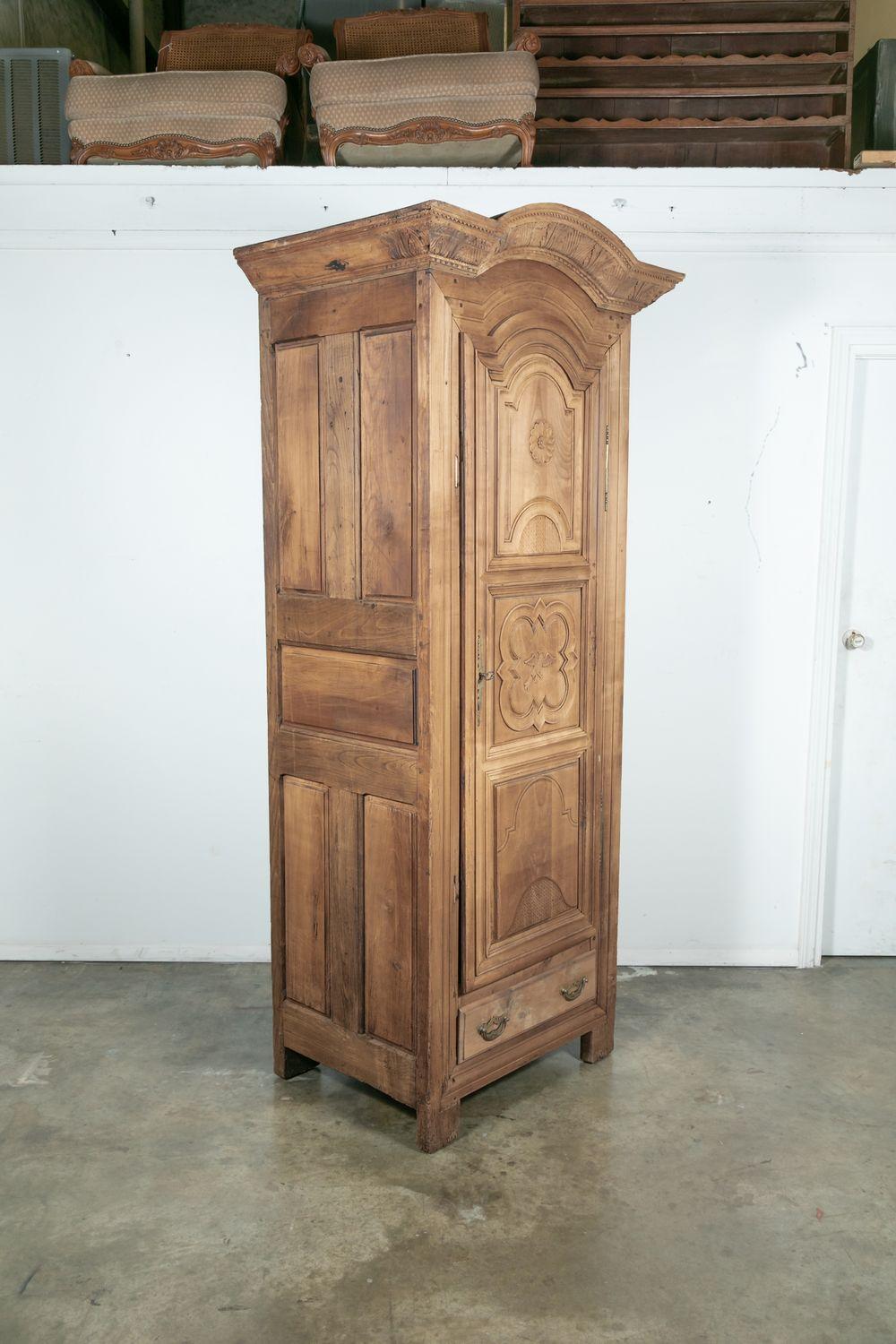 18th century French Louis XIV style bonnetiere (one door armoire) handcrafted in walnut by master artisans in the Normandy region, circa 1750s. The single door bleached armoire, having a chapeau de gendarme cornice, sits on block feet and features a