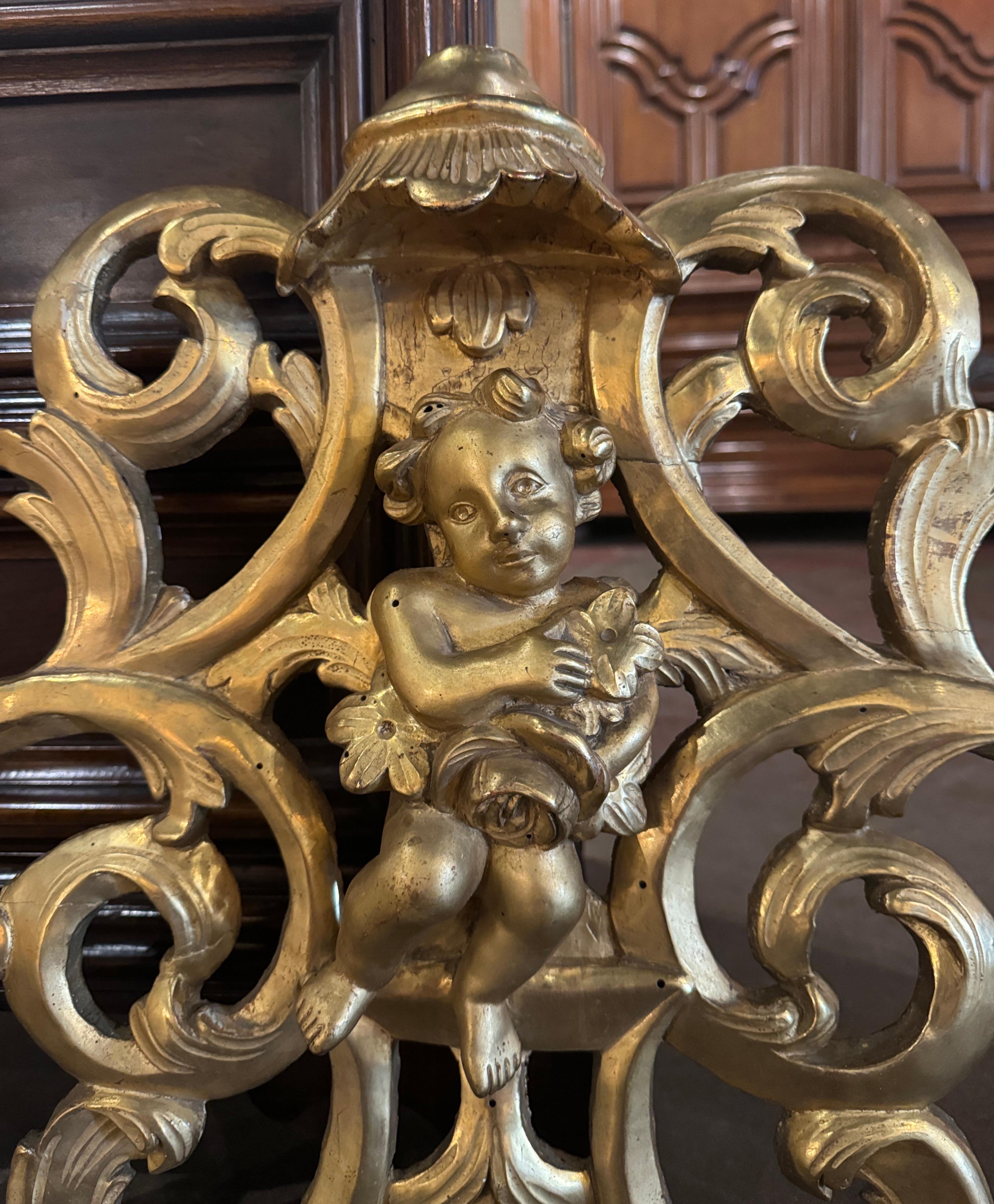 Decorate a wall or dress a over-door with this elegant antique gilt carving. Crafted in Provence, France circa 1780, the element features a center cherub sculpture holding a flower bouquet and flanked with pierced scrolled motifs of acanthus leaves.