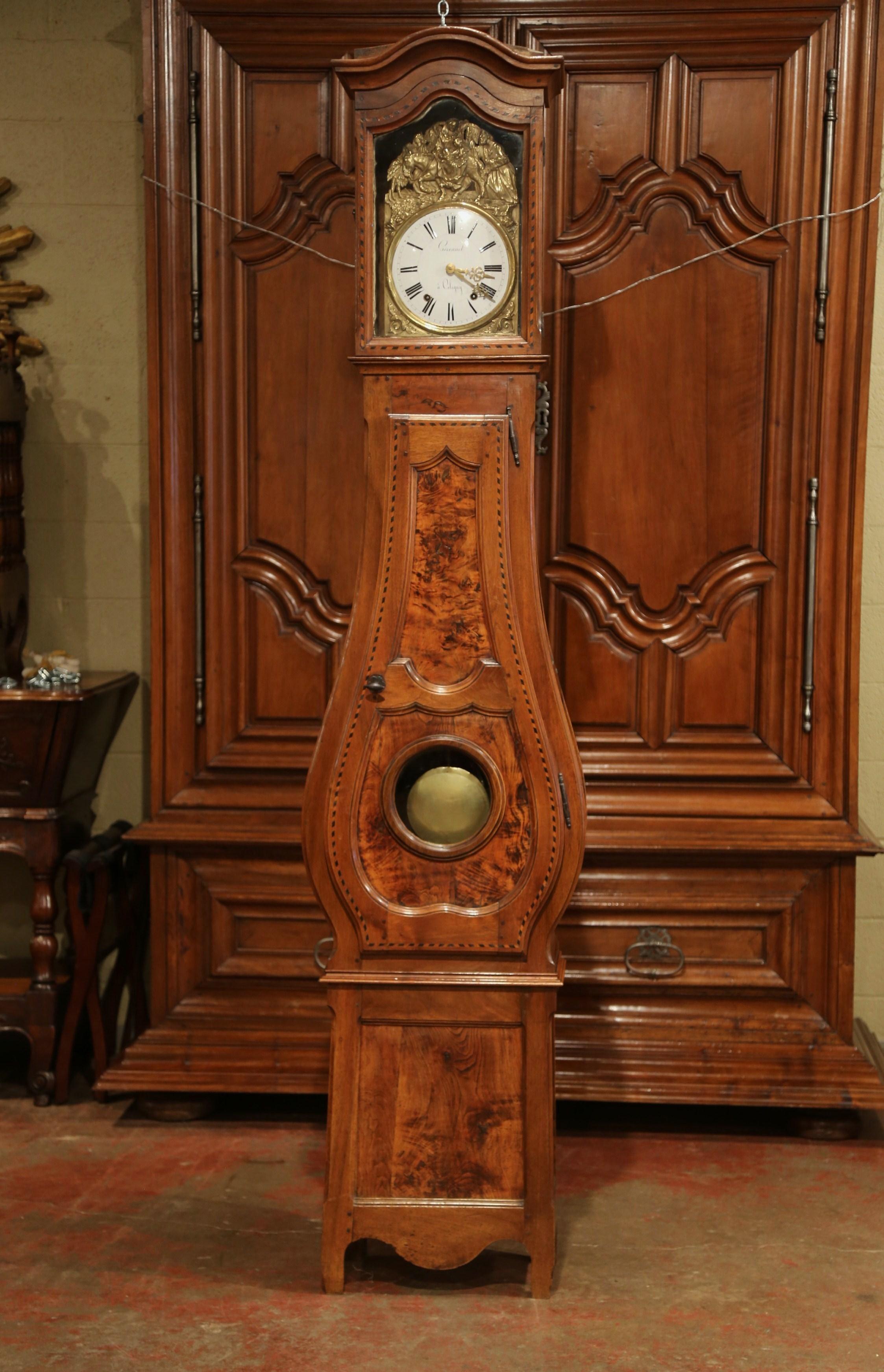 Crafted in lyon, France, circa 1780, the antique fruitwood tall case clock features beautiful carved lines including a bonnet top, a violin shape body style and scrolled feet under a scalloped apron at the base; it is further embellished with
