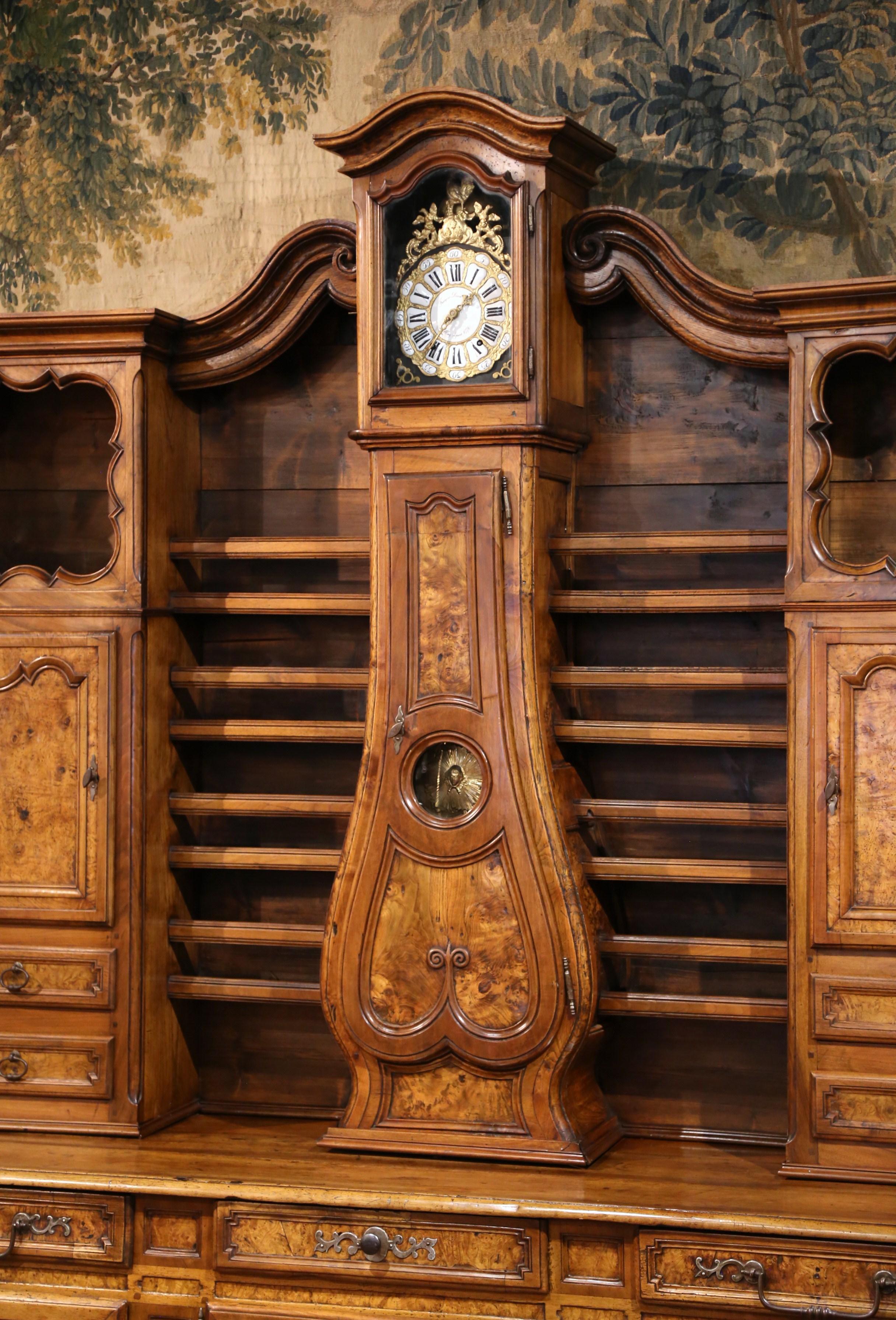Hand carved in Southern France circa 1760, the large display cabinet decorated with floral and leaf motifs throughout, is built in two sections. The top part with volutes features a bonnet top over the clock casing with glass, a violin shape center